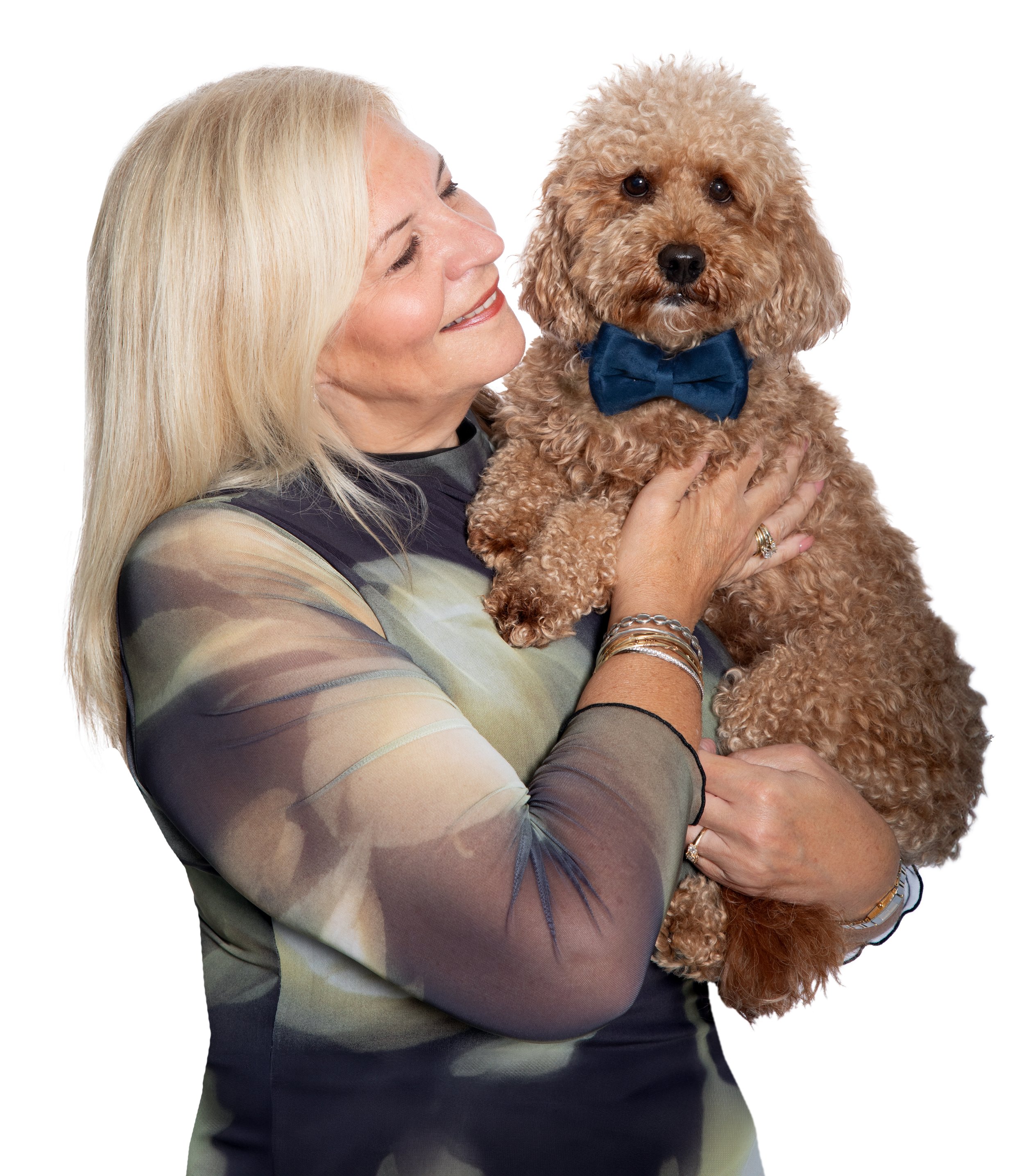 A woman with long blonde hair smiling and holding a curly-haired dog with a blue bow tie.