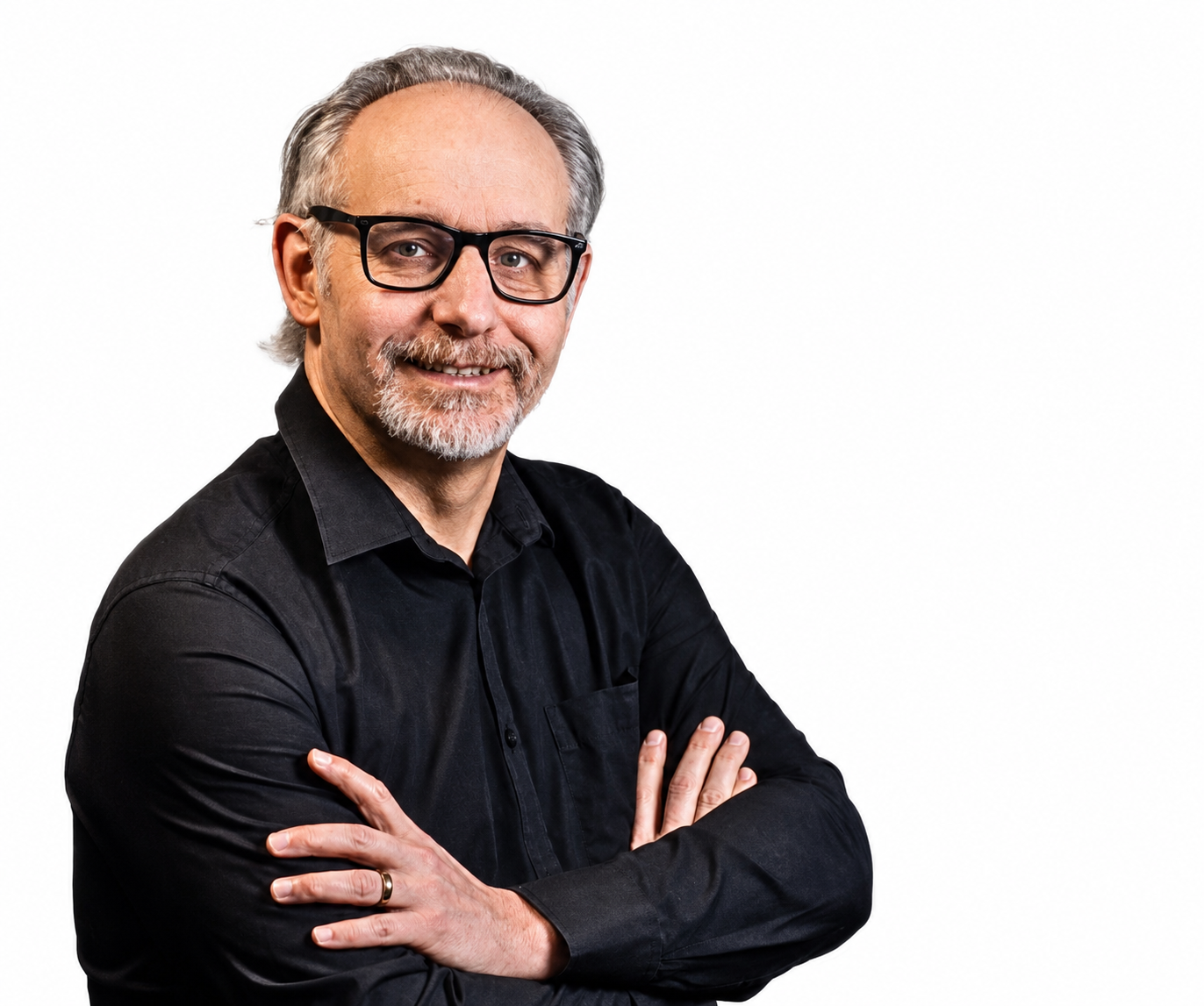 A smiling middle-aged man with gray hair, glasses, and a beard, wearing a black shirt with arms crossed, standing against a plain white background.