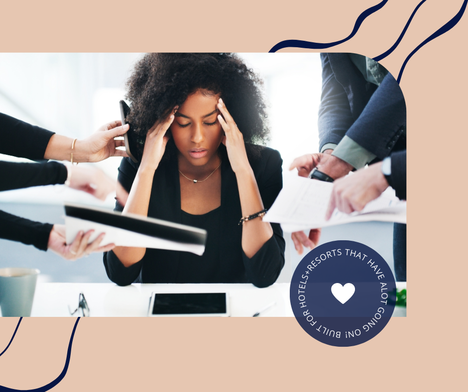 A woman appears stressed, holding her forehead with both hands, surrounded by several people offering documents and a phone in a busy office environment.