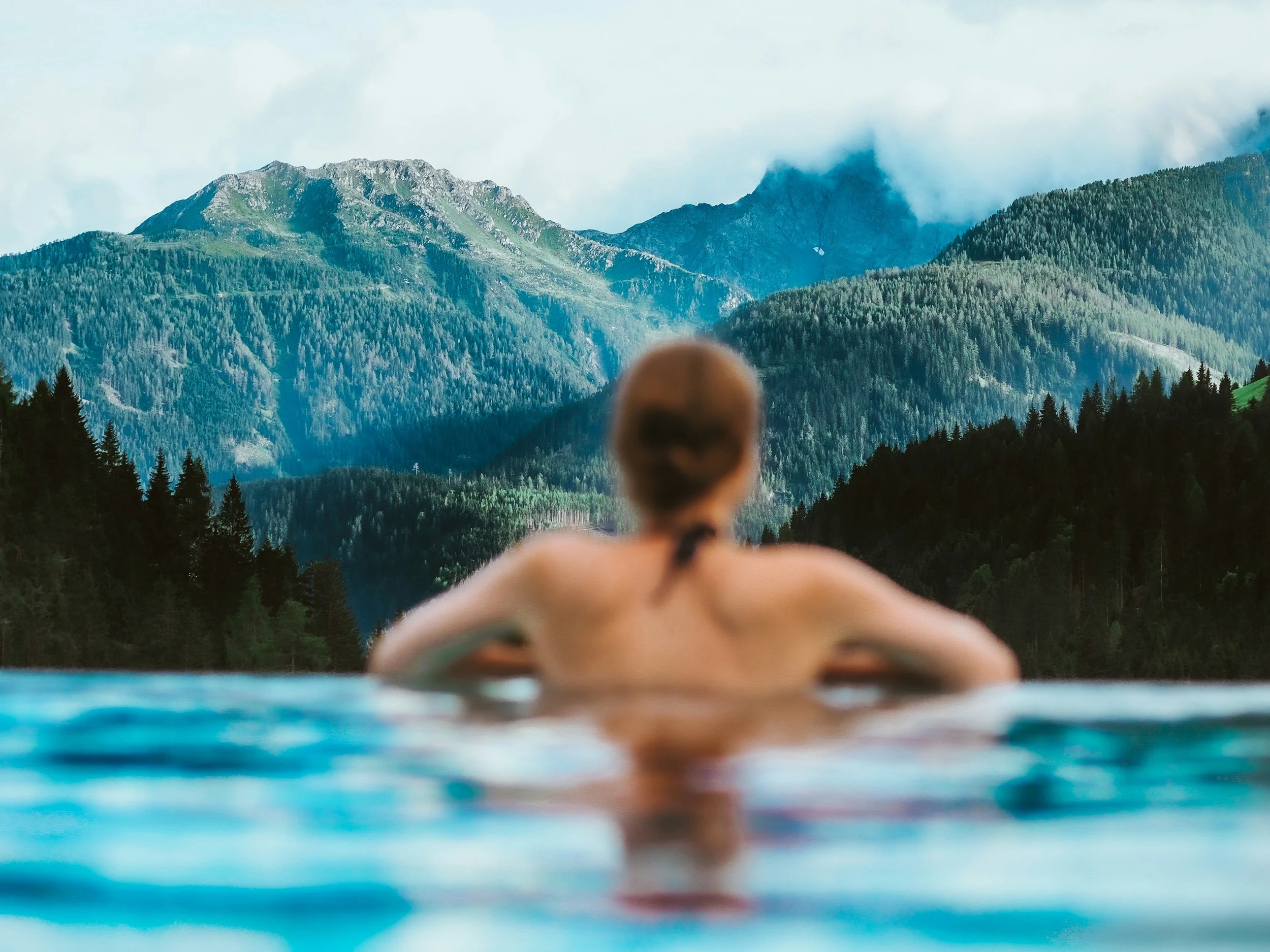 A person swimming in a pool with mountain scenery in the background.