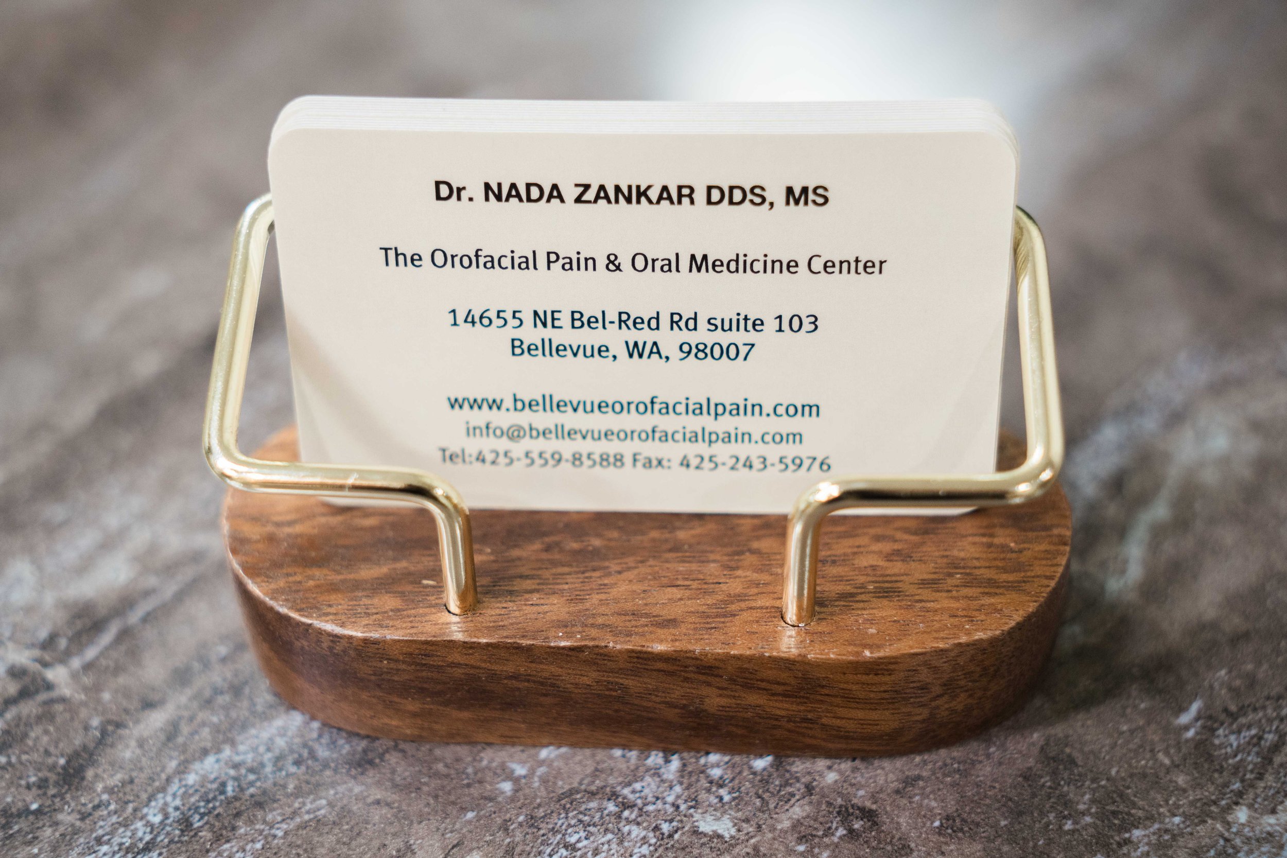 Business card for Dr. Nada Zankar DDS, MS at The Orofacial Pain & Oral Medicine Center with address in Bellevue, Washington, placed on a wooden stand.