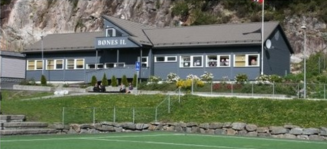 En blå bygning med en skilt som sier 'Bones IL' ved sjøen, omgitt av grønt gress og rastebenker.