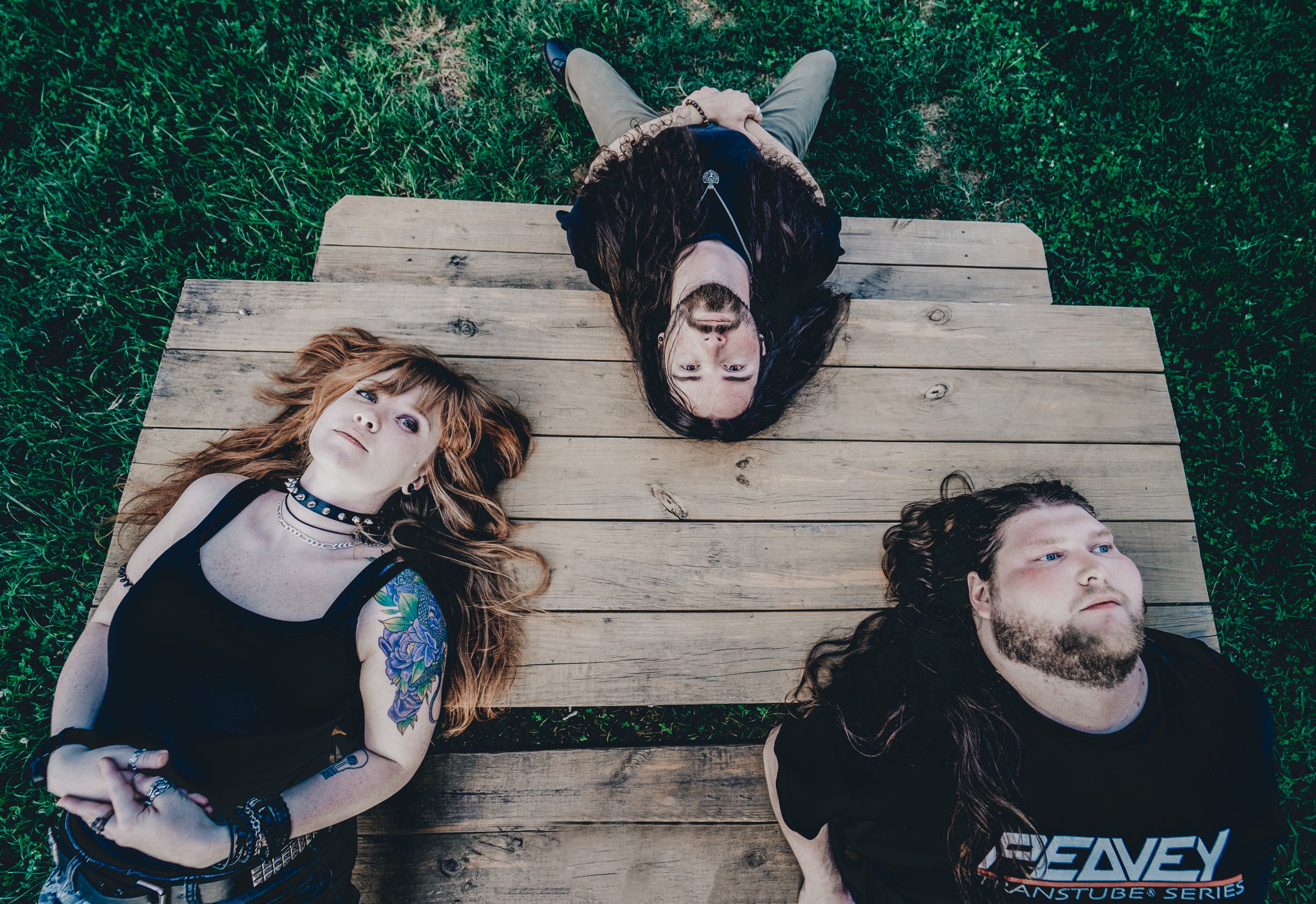 Four people lying on a wooden dock on grass, viewed from above. Two women and two men, all young adults, are relaxing with their eyes open.