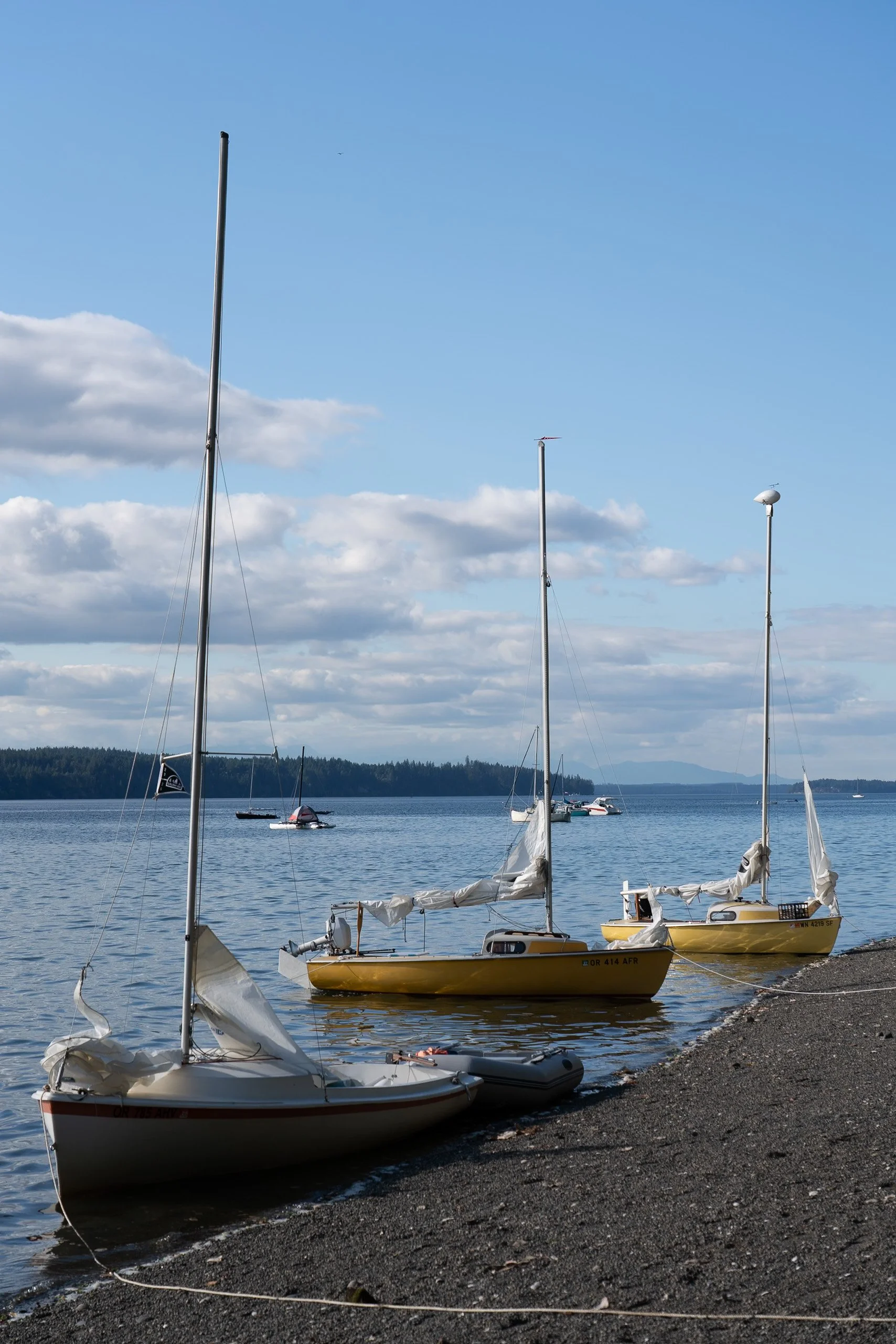 Sailboats on a calm lake with a rocky shore, under a partly cloudy sky.