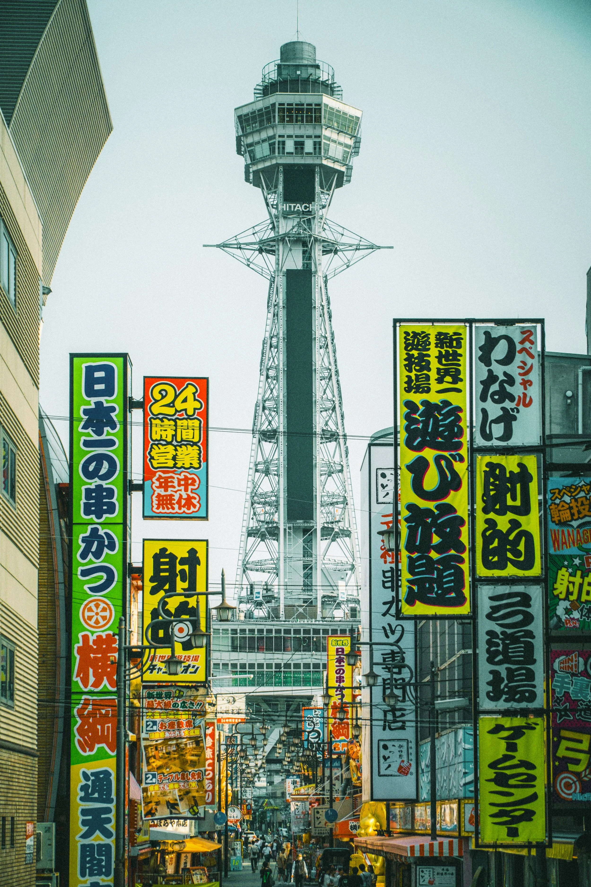 Vue urbaine à Tokyo avec une tour d'observation en arrière-plan et de nombreux panneaux publicitaires en japonais dans la rue.
