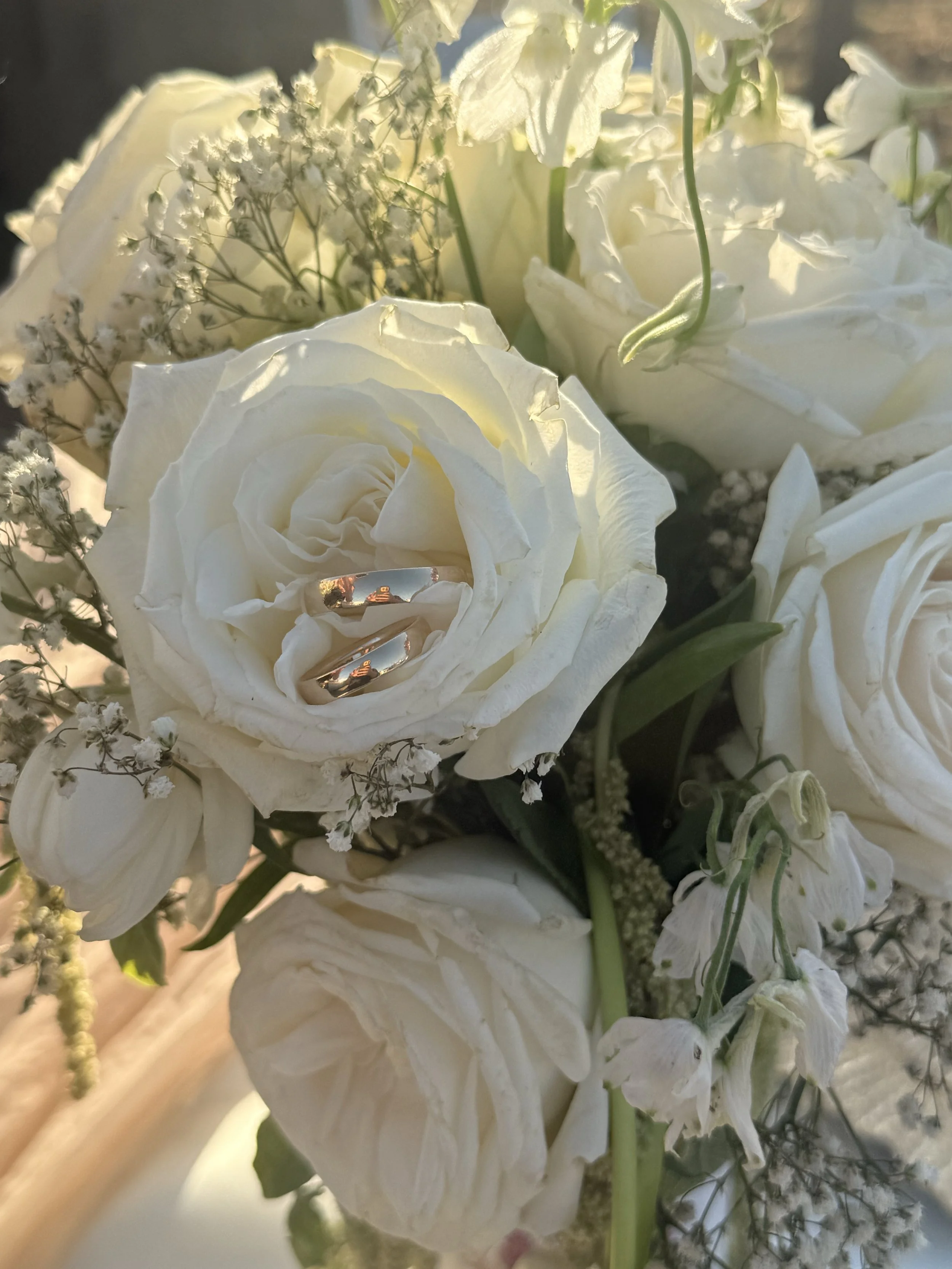 Close-up of a white roses bouquet with two wedding rings placed inside one of the roses.