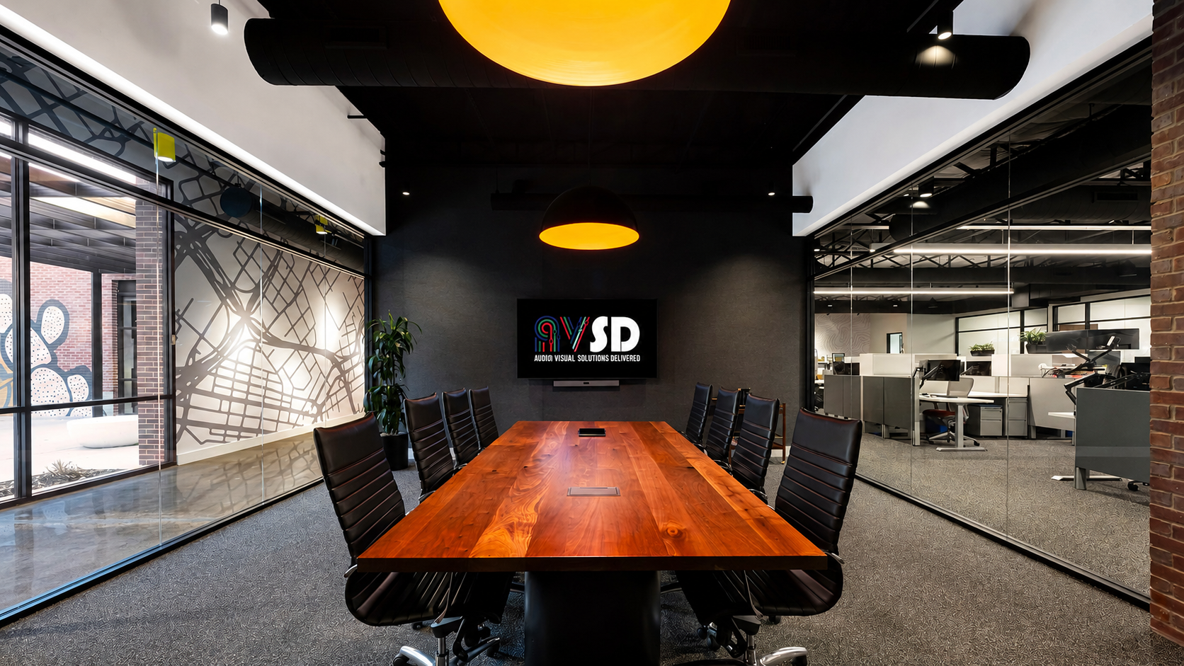 Modern conference room with a long wooden table, black office chairs, a wall-mounted screen displaying 'R9 VSD Audio Visual Solutions Delivered,' large windows with decorative frosted patterns, and an adjacent open office space visible through glass 