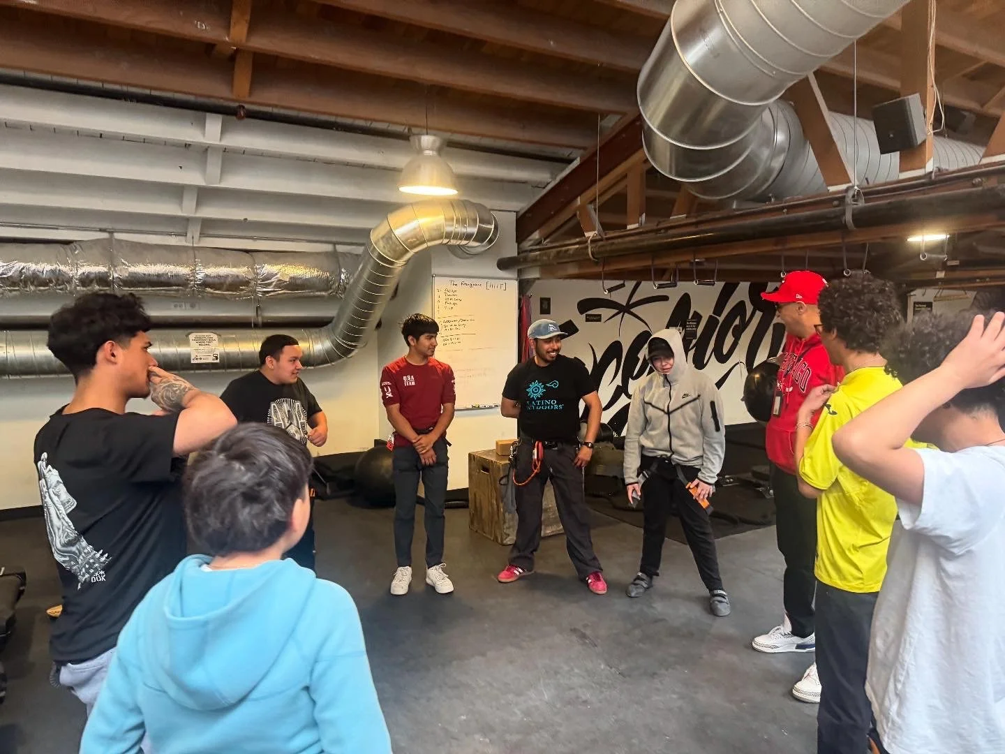 Group of people gathered in a gym or fitness studio, listening to an instructor during a fitness class.