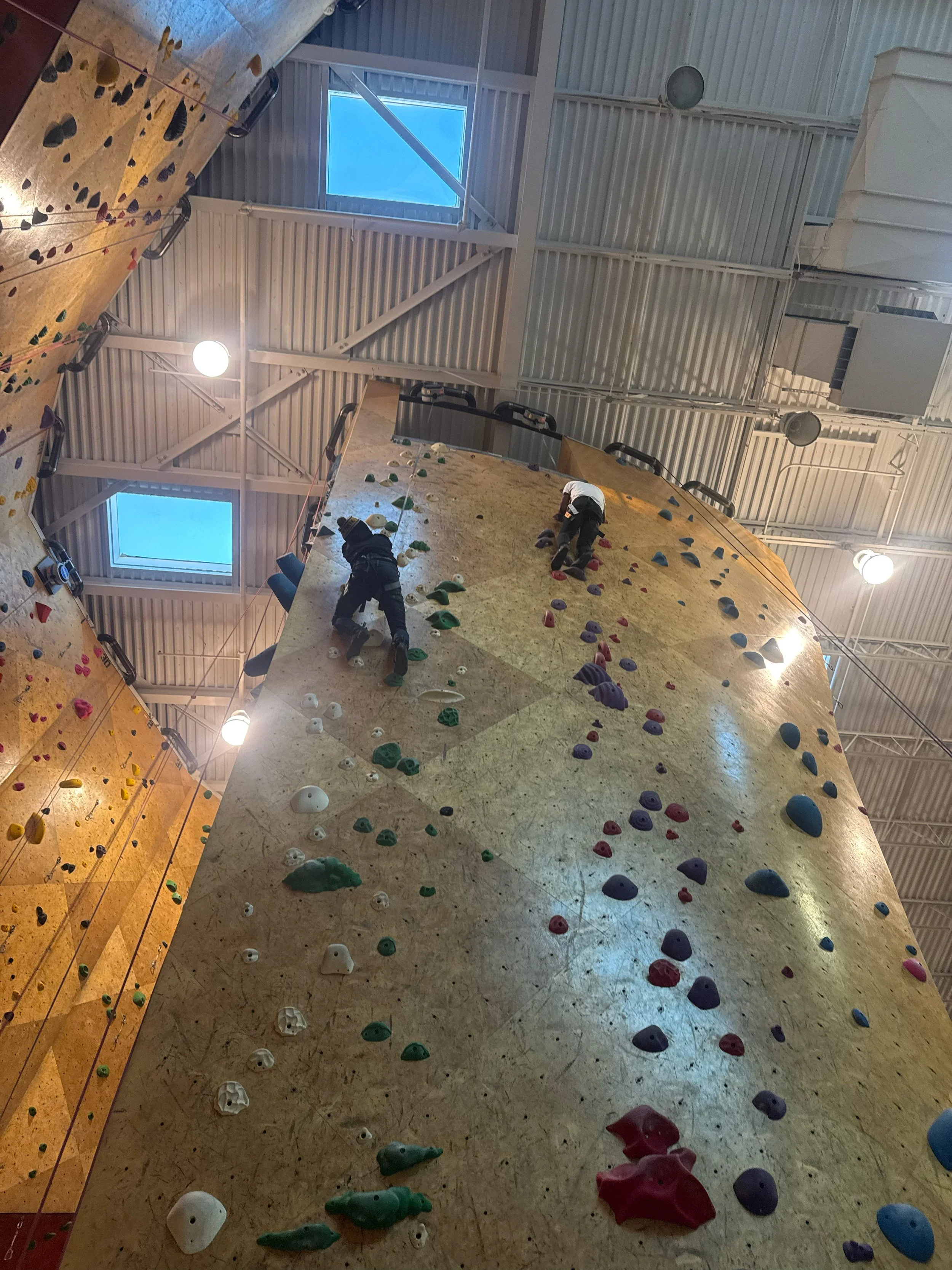 Indoor rock climbing gym with two people climbing on a variety of colored climbing holds on the walls.
