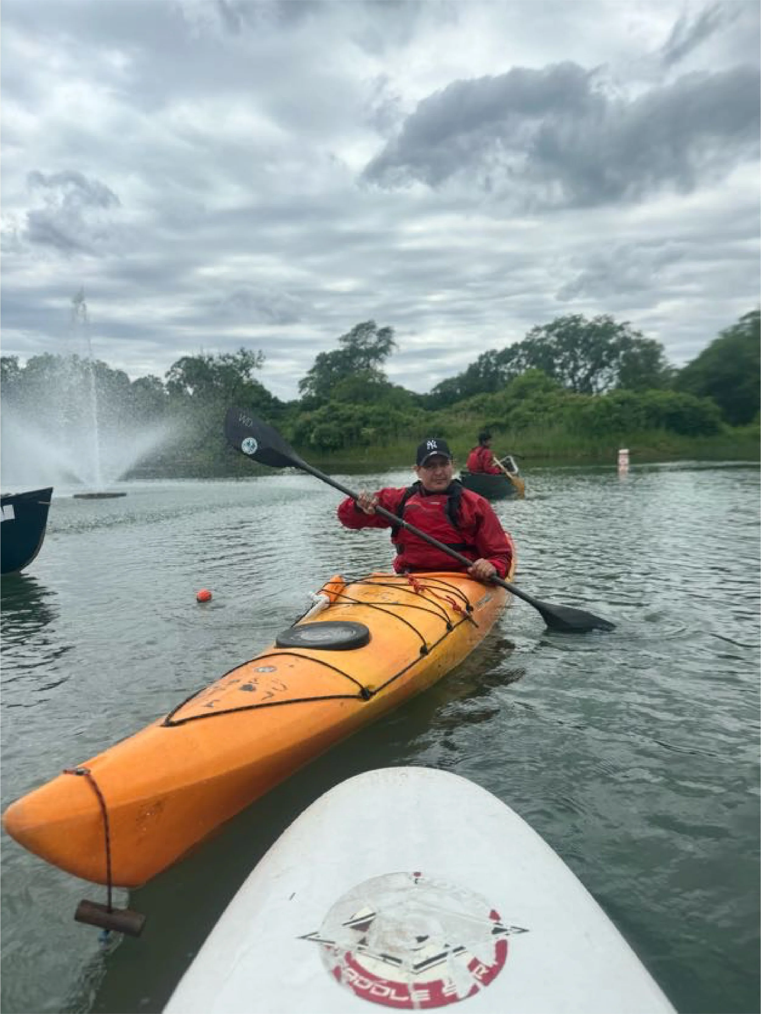 People kayaking on a river or lake during cloudy weather, surrounded by trees.