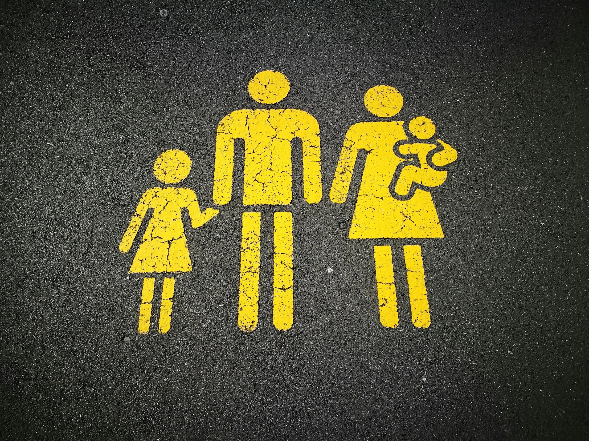 Yellow pedestrian symbol on the pavement depicting a family of four, including two adults and two children.