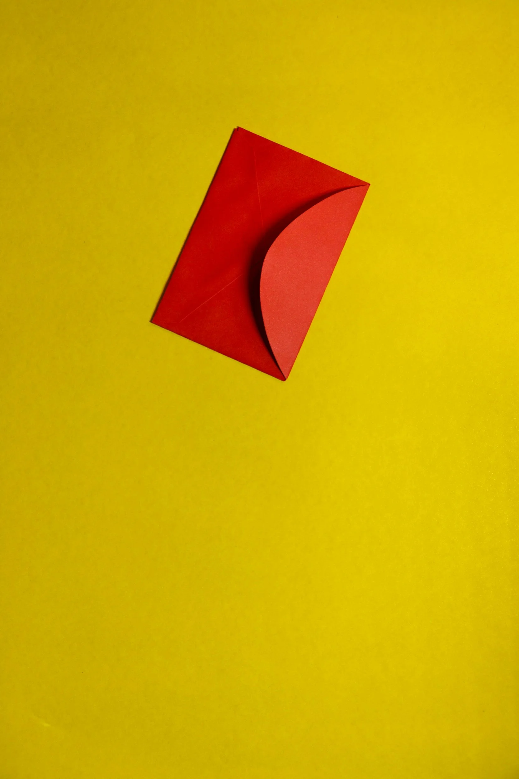A red paper sculpture on a yellow surface, shaped like a curved crescent within a cube.