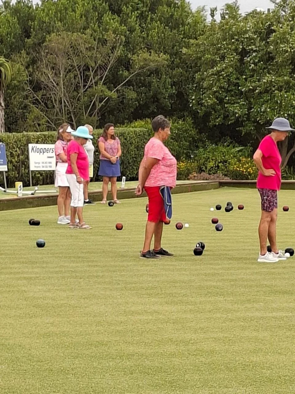 People playing pétanque on a grassy field with trees in the background