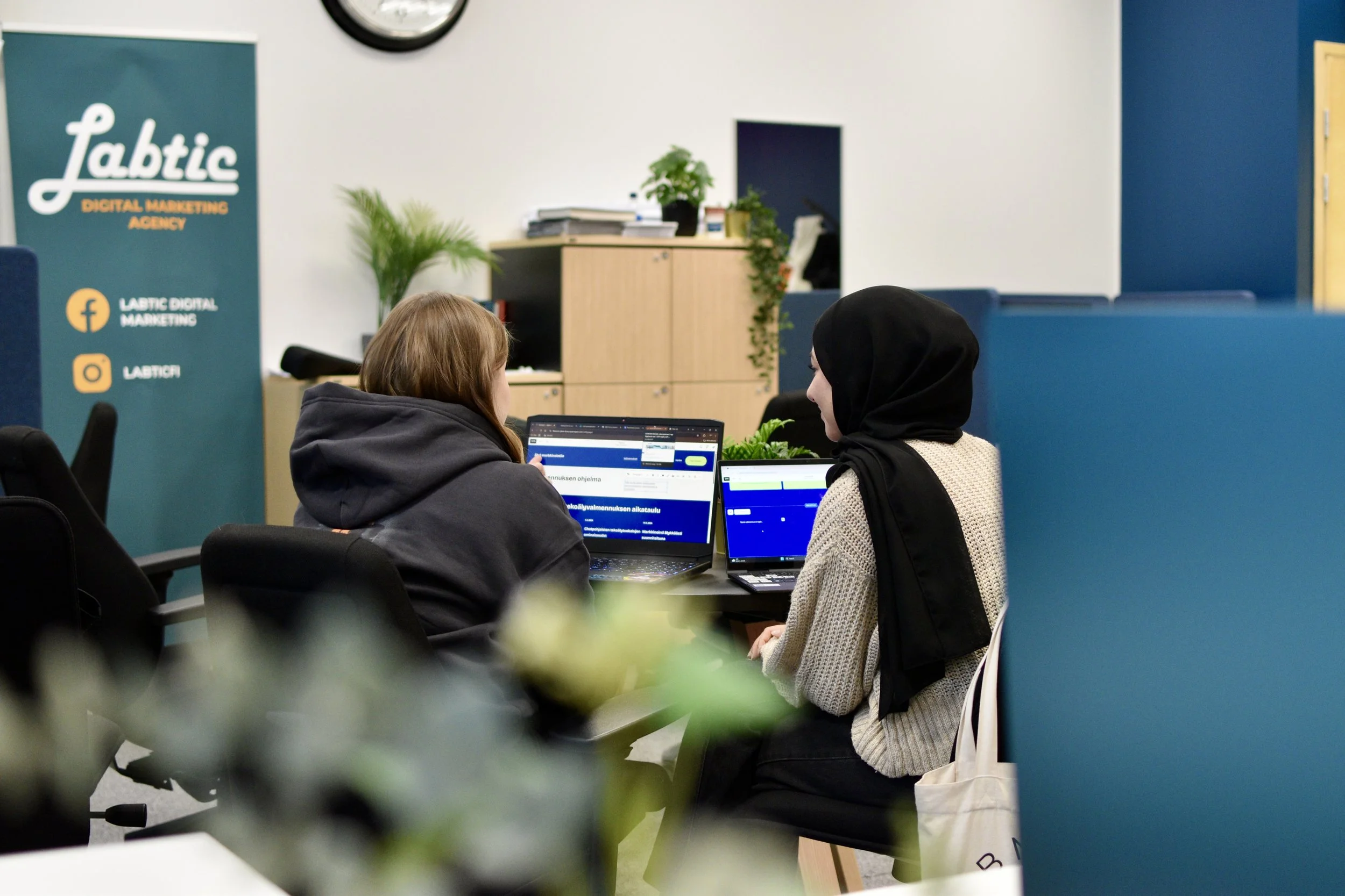 Kaksi opiskelijaa pöydän ääressä työstämässä projektia tietokoneilla.