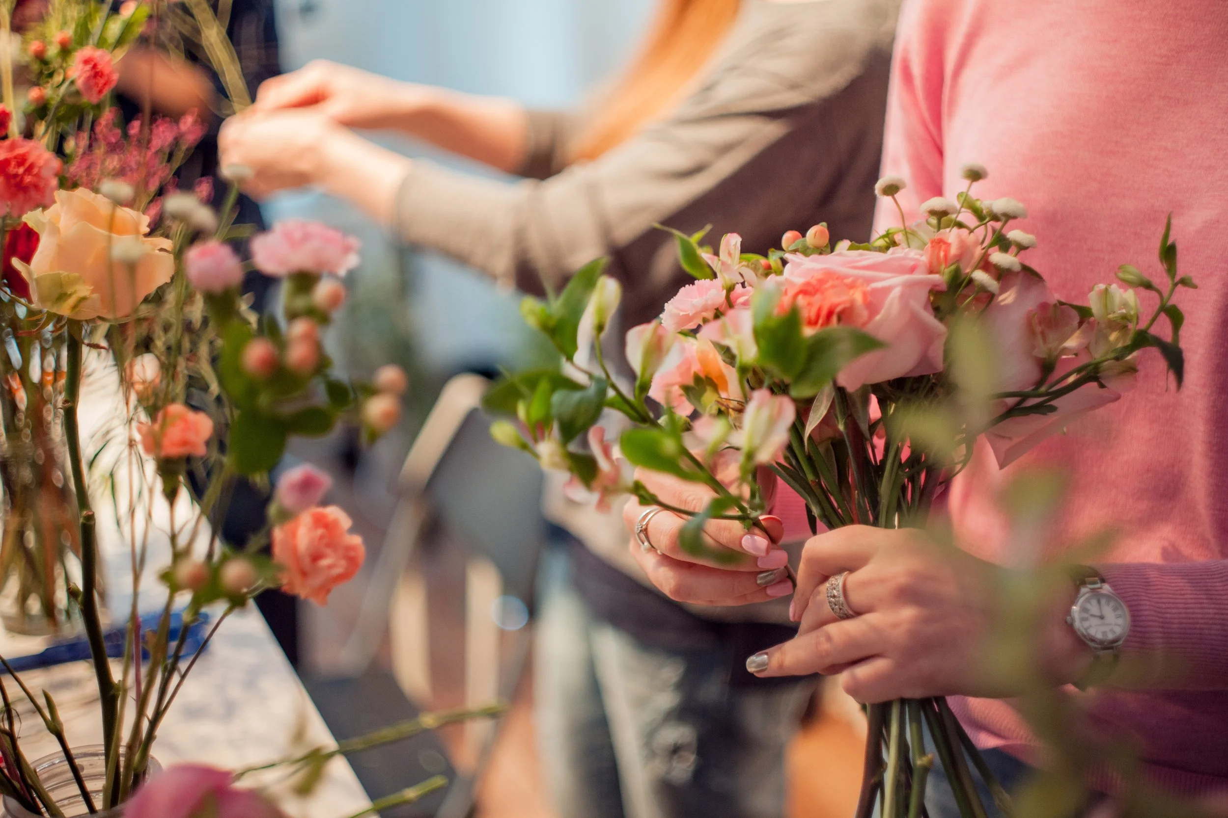 Person holding pink and peach flowers in a flower shop.