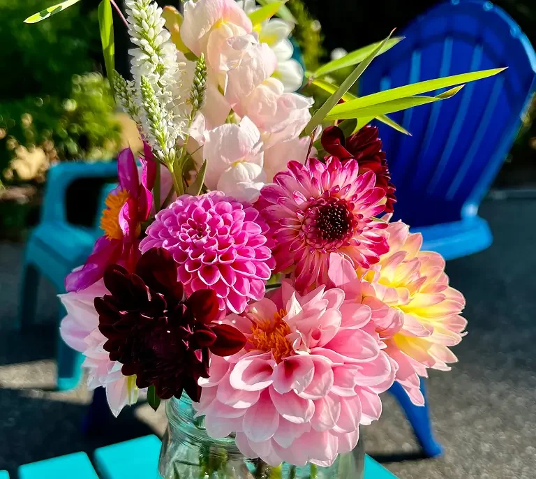 Assorted pink, purple, and white flowers in a glass jar with a blue chair in the background.