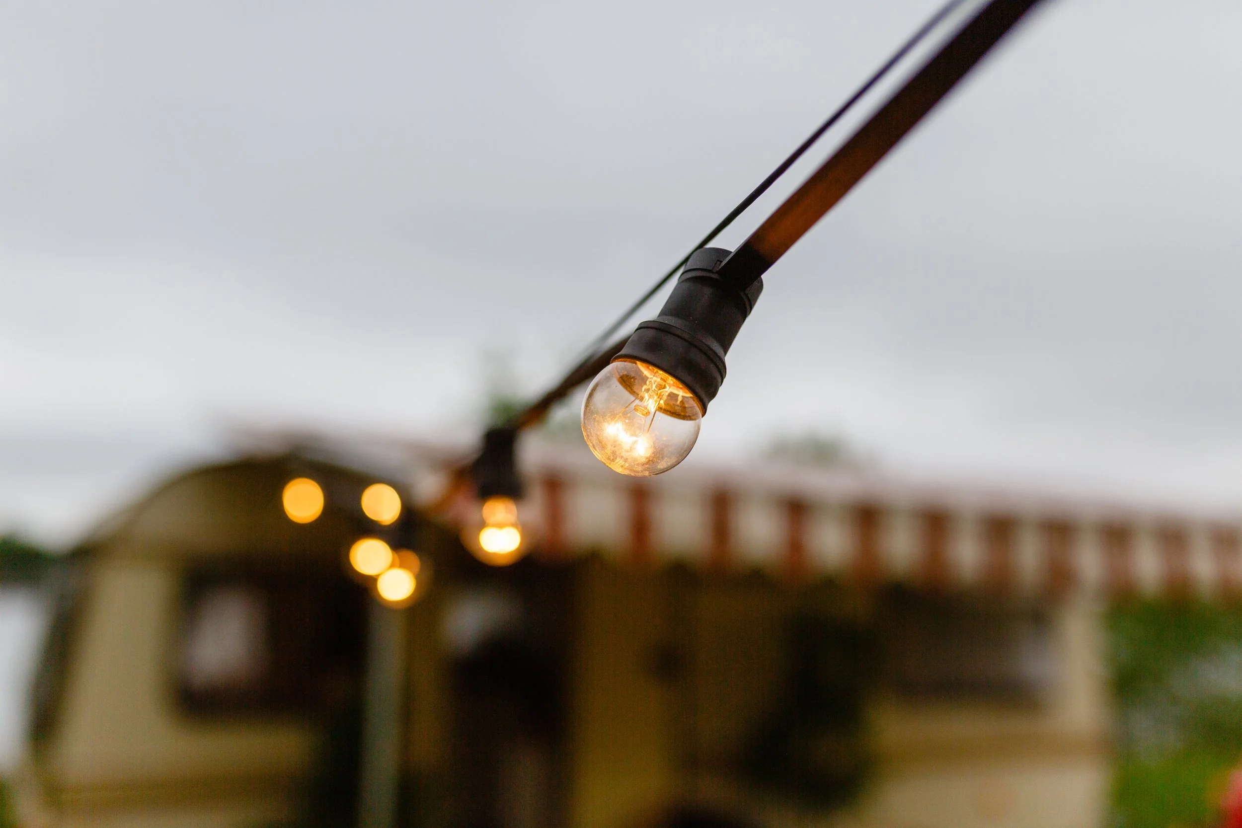 Close-up of a string of outdoor string lights with one illuminated bulb in focus and the background blurred.