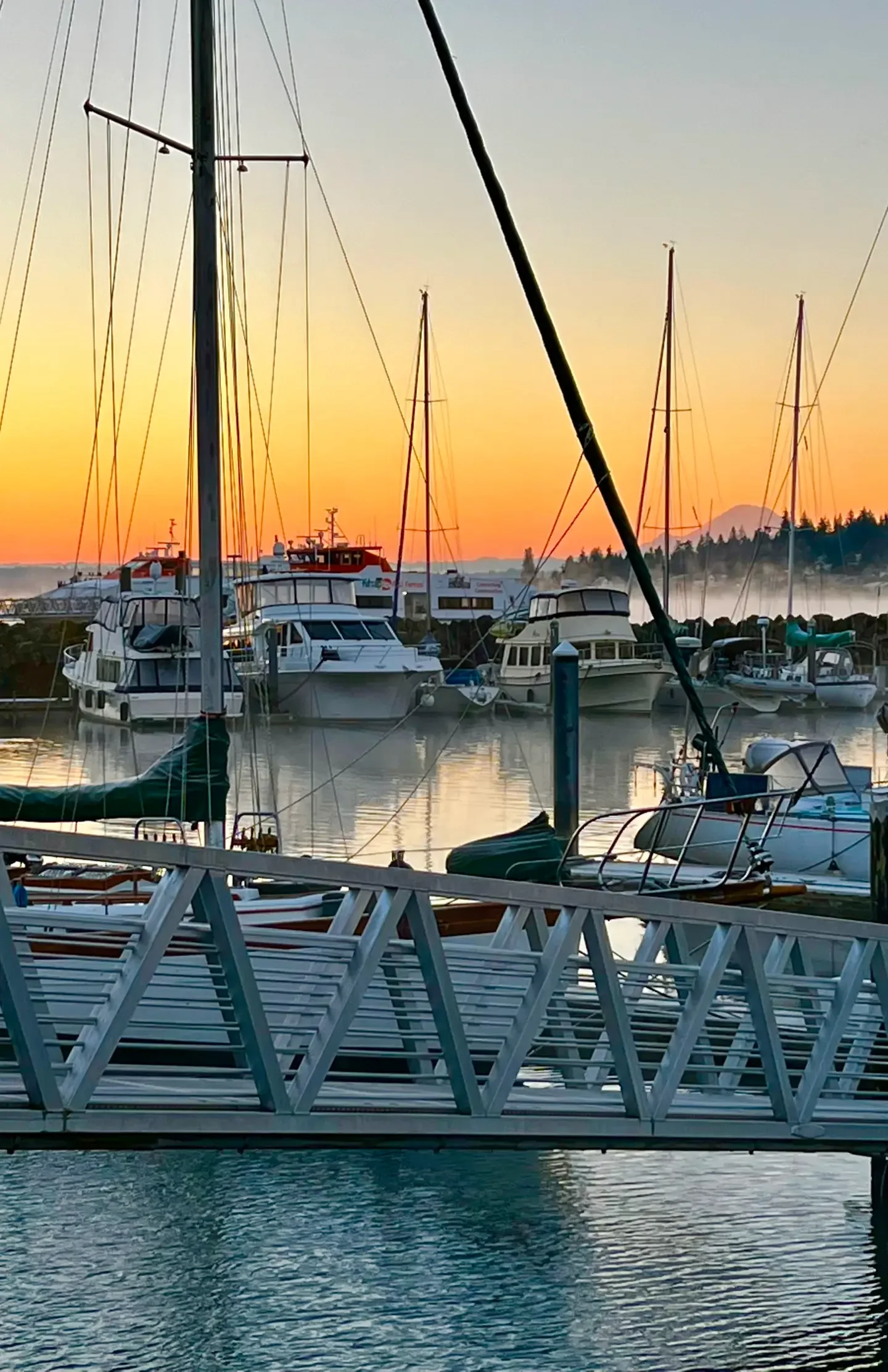 A marina with several boats docked, a wooden dock in the foreground, and a sunset with a colorful sky in the background.