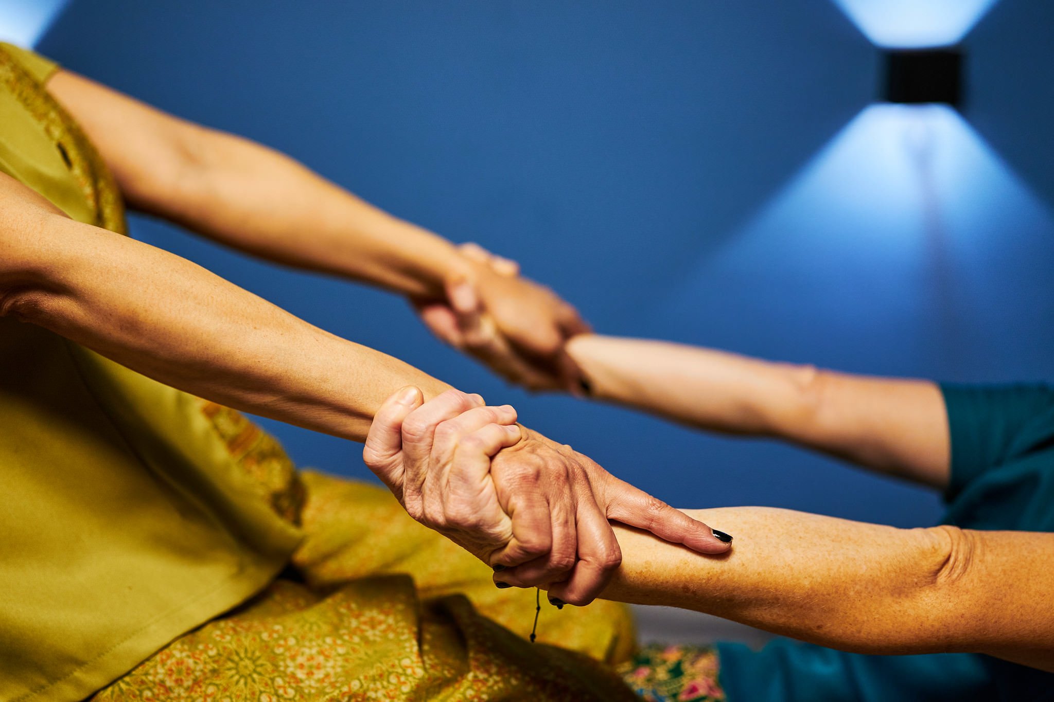 Elderly woman and middle-aged woman holding hands, possibly at a social gathering or dance class.