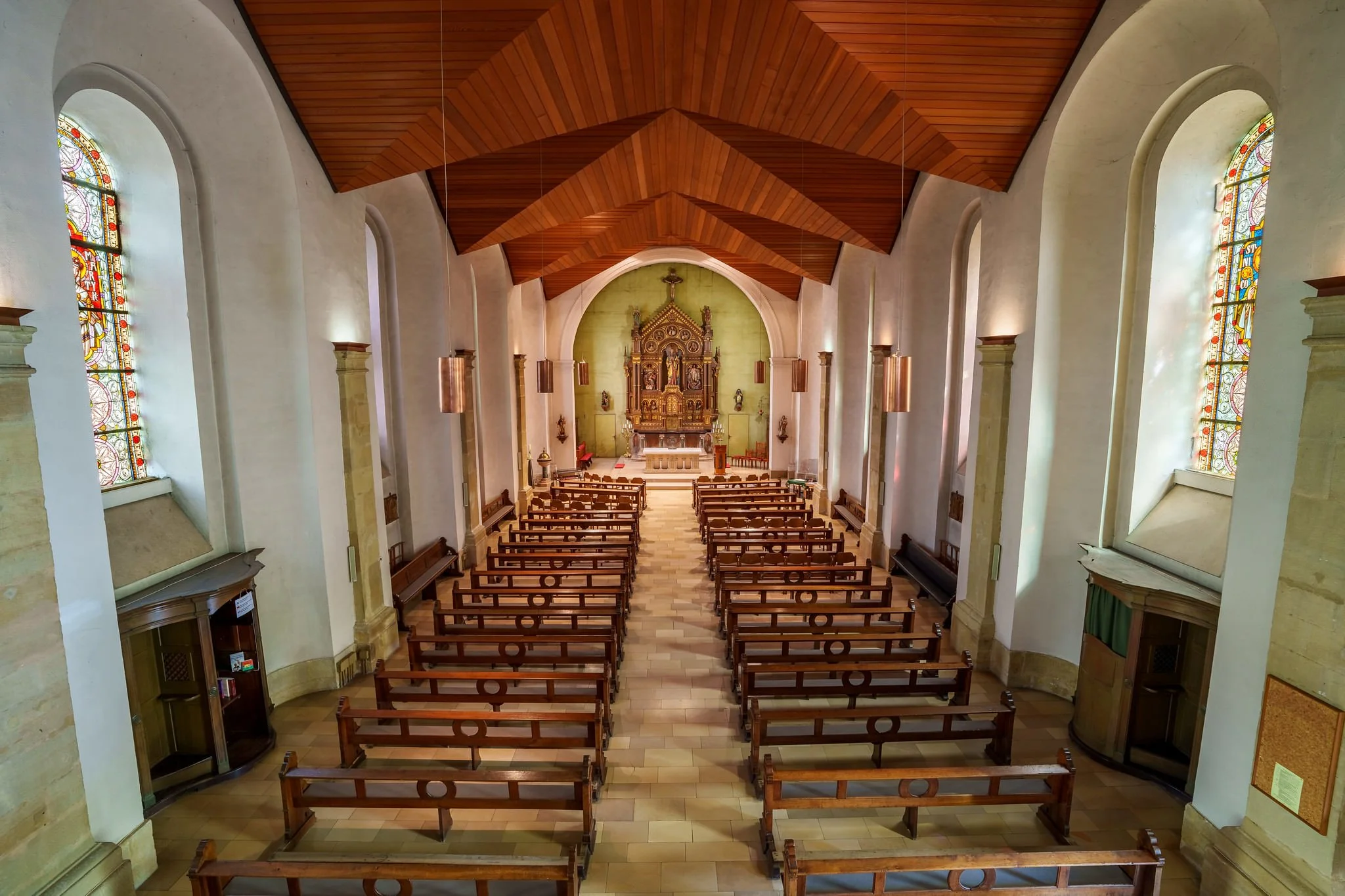 Interior of a church with wooden ceiling, stained glass windows, wooden pews, and an altar at the front.