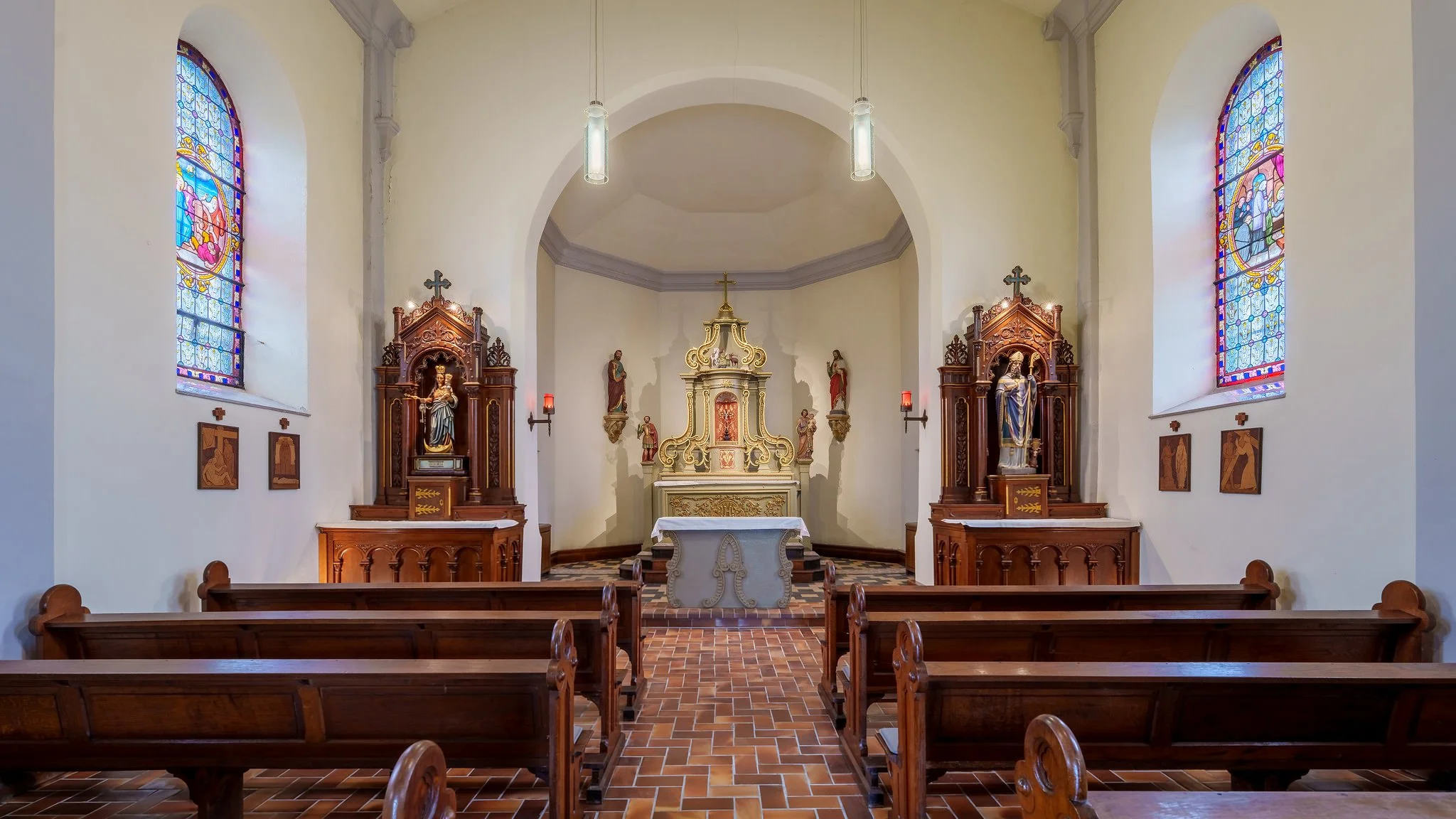 Interior of a small church with stained glass windows, wooden pews, and an altar with religious statues and artwork.