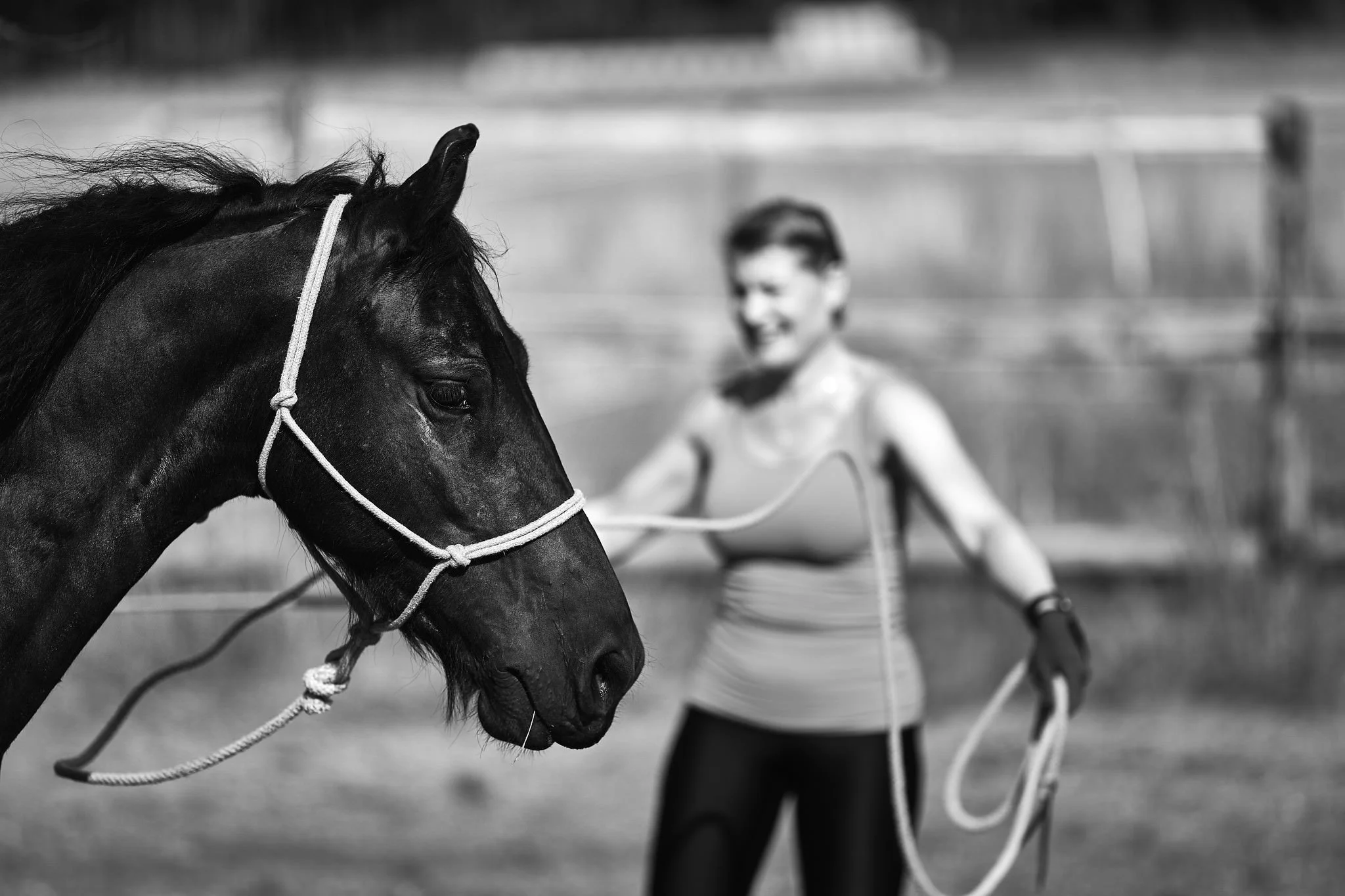 Black and white photo of a person riding a horse on a racetrack with a blurry horse in the background.