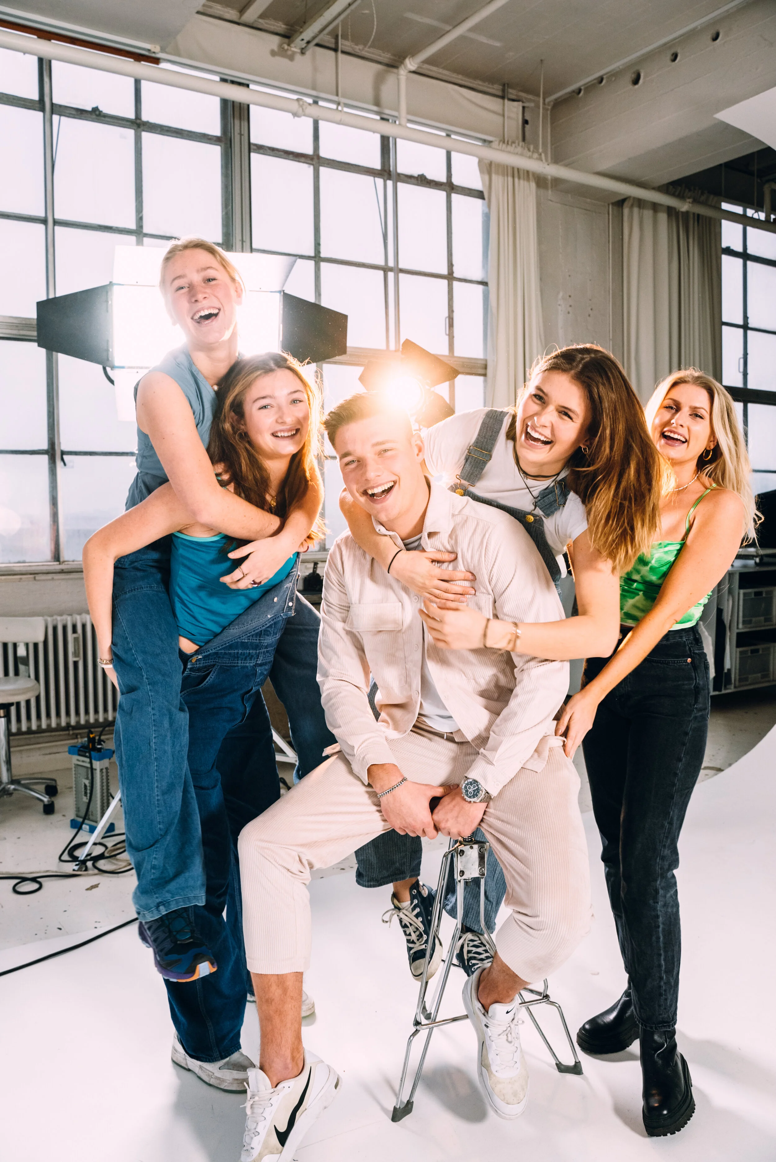 A group of five young people laughing and having fun in a photography studio with bright lighting and large windows.