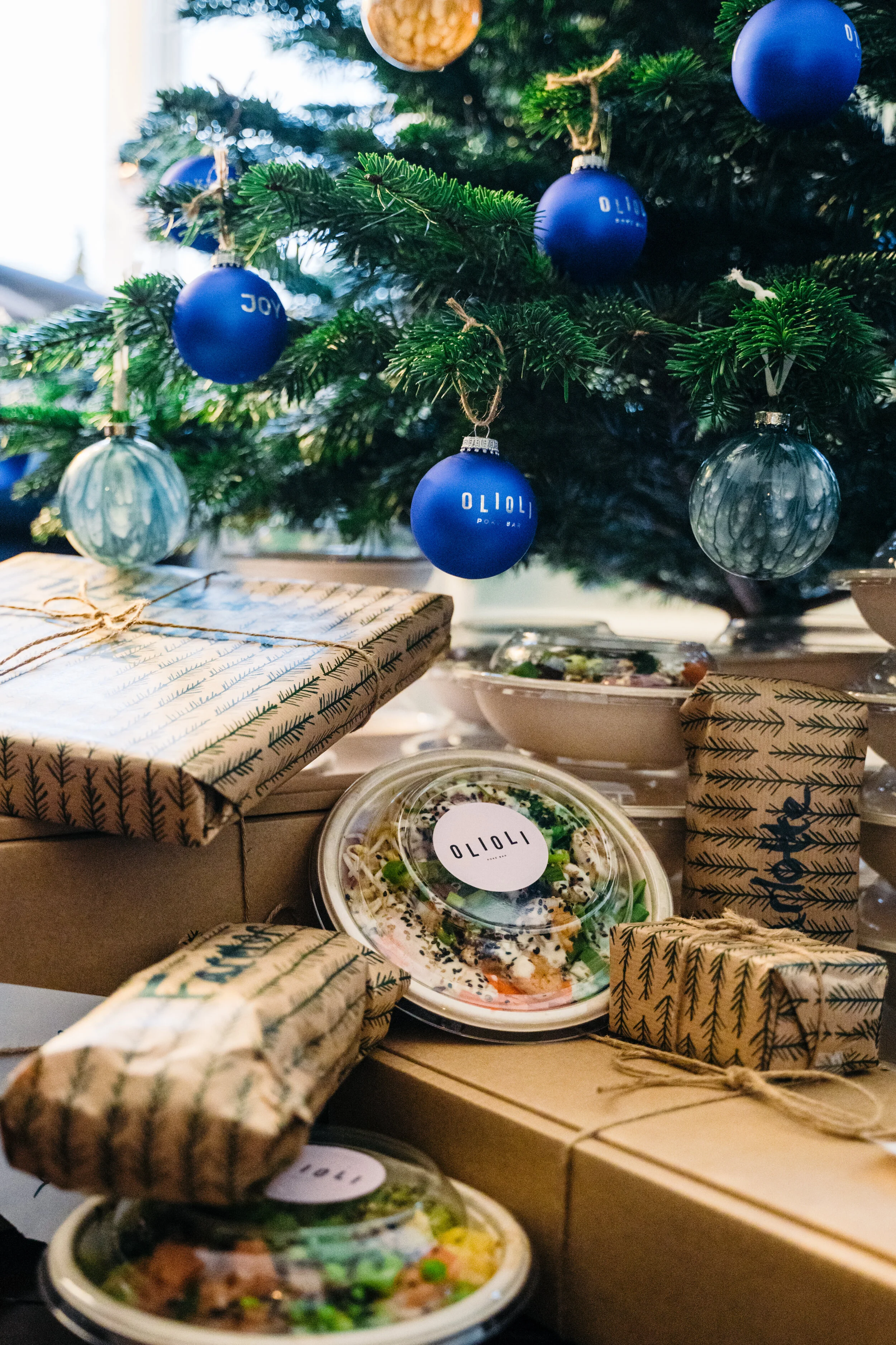 Decorated Christmas tree with blue ornaments and presents underneath, including takeout food containers.