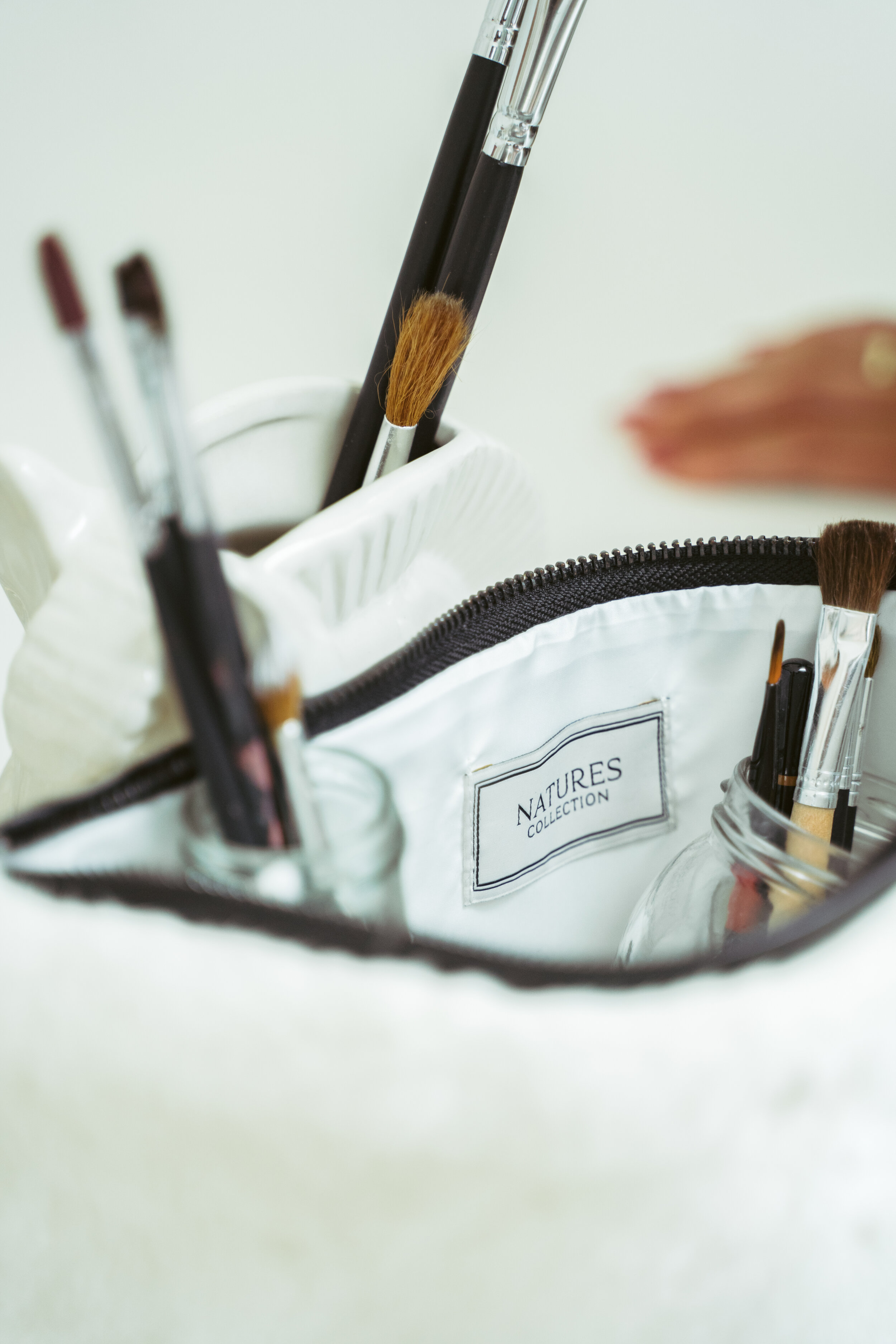 Close-up of a white makeup bag labeled 'NATURES COLLECTION' with various brushes and tools inside.