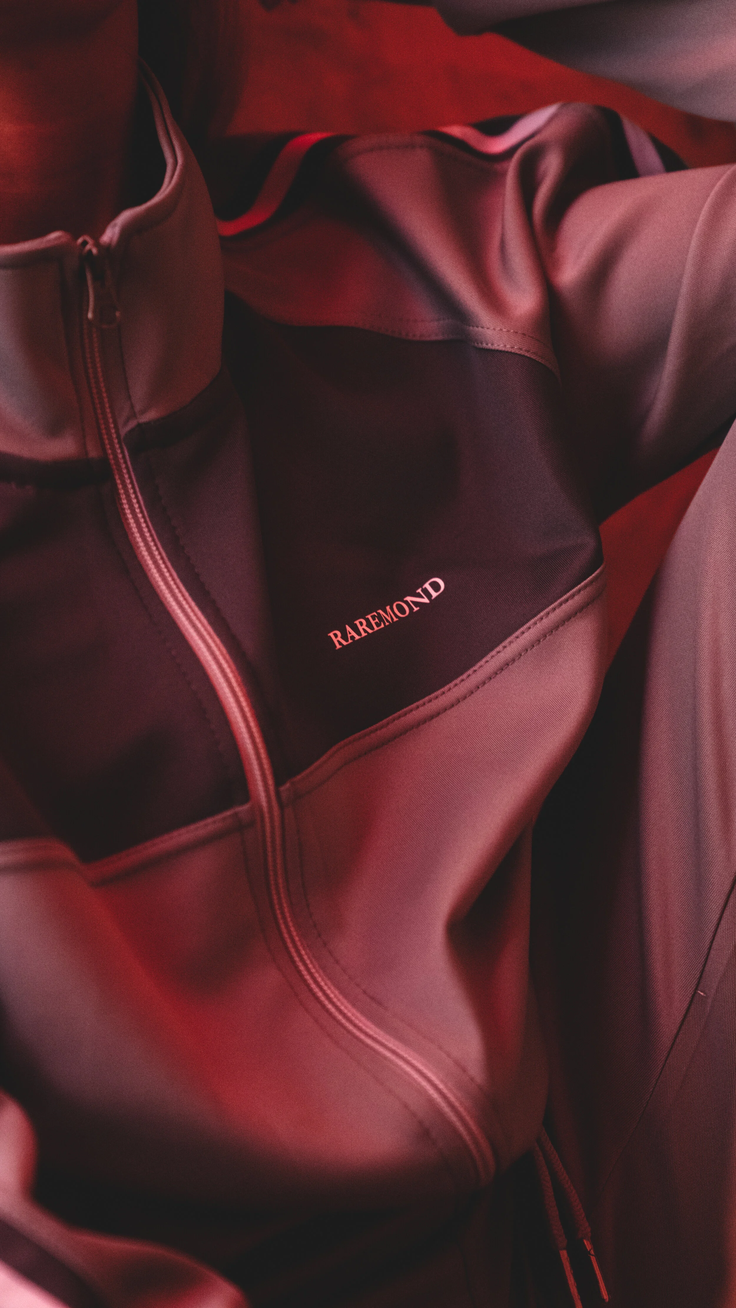 Close-up of a burgundy jacket with a black pocket that has the word "RAREMOND" embroidered in pink.