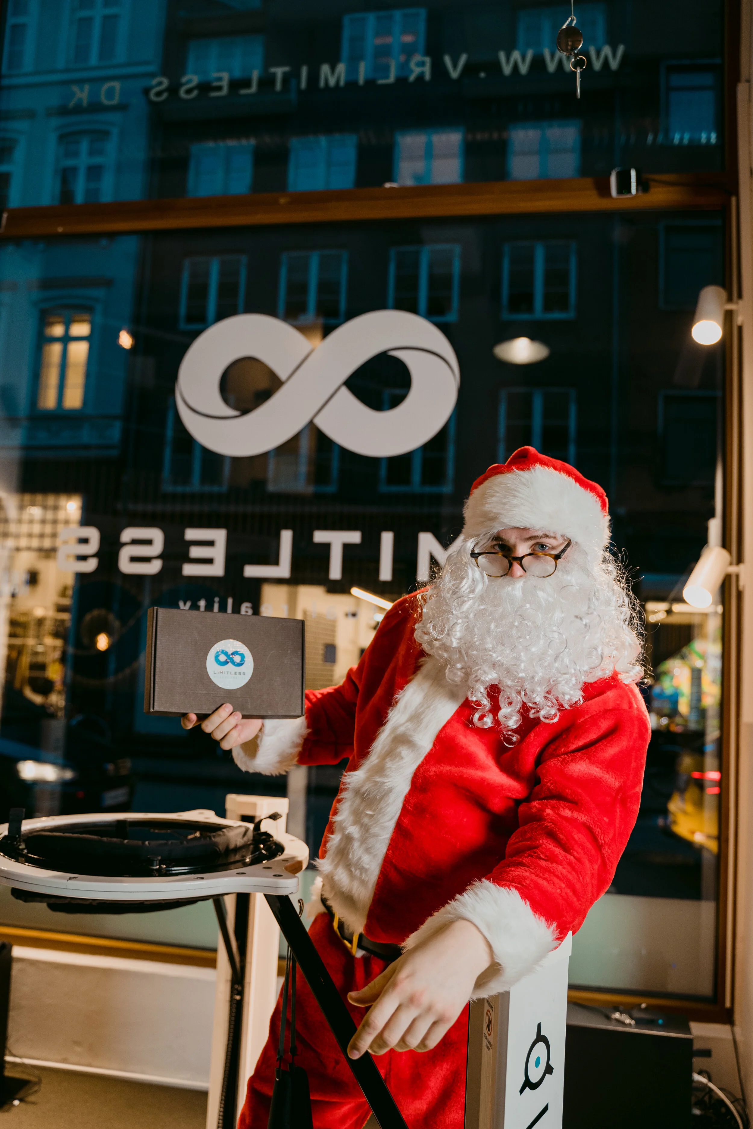 Person dressed as Santa Claus holding a small box inside a store with a large window in the background.