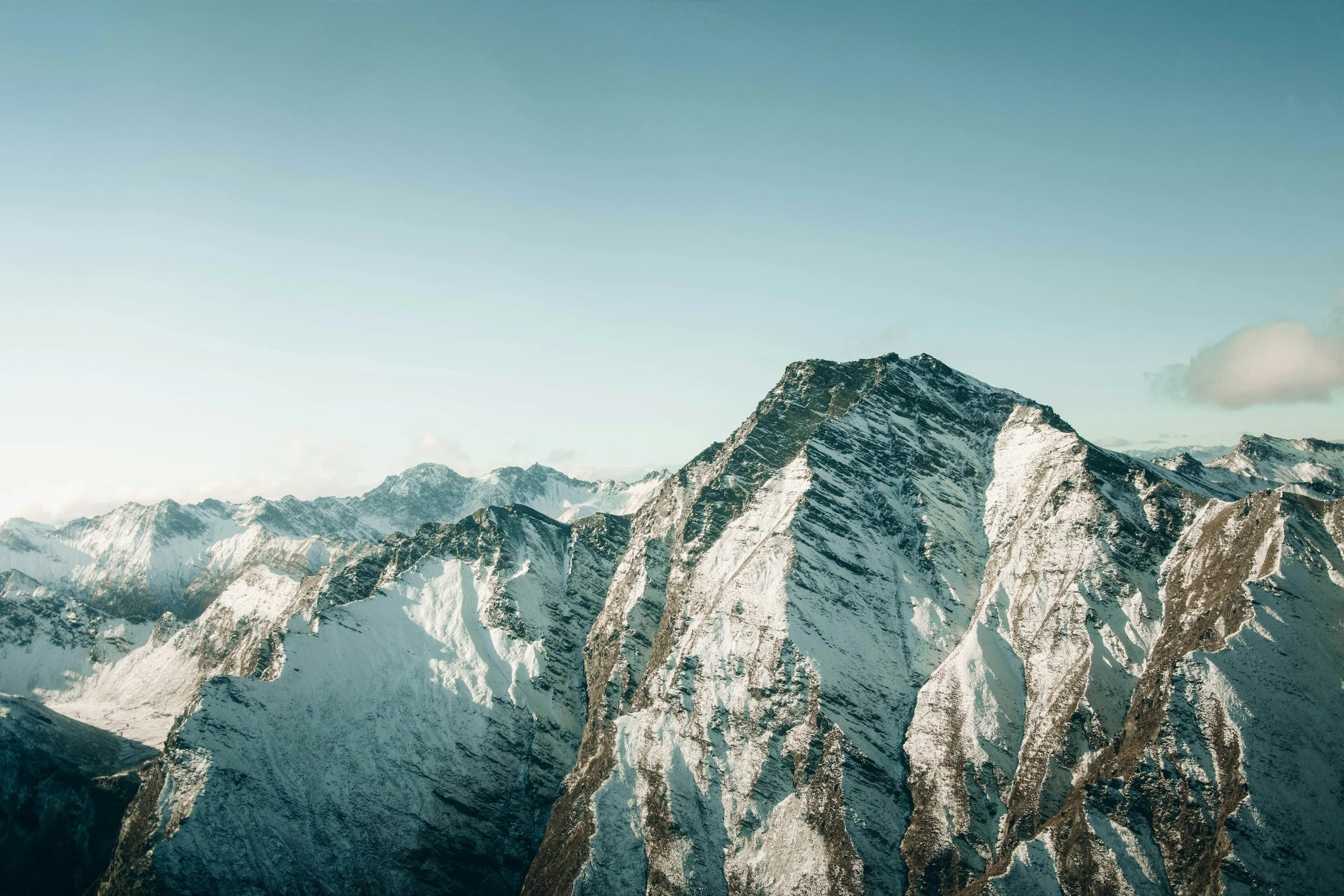 Snow-capped mountain range under a clear sky with a few clouds.