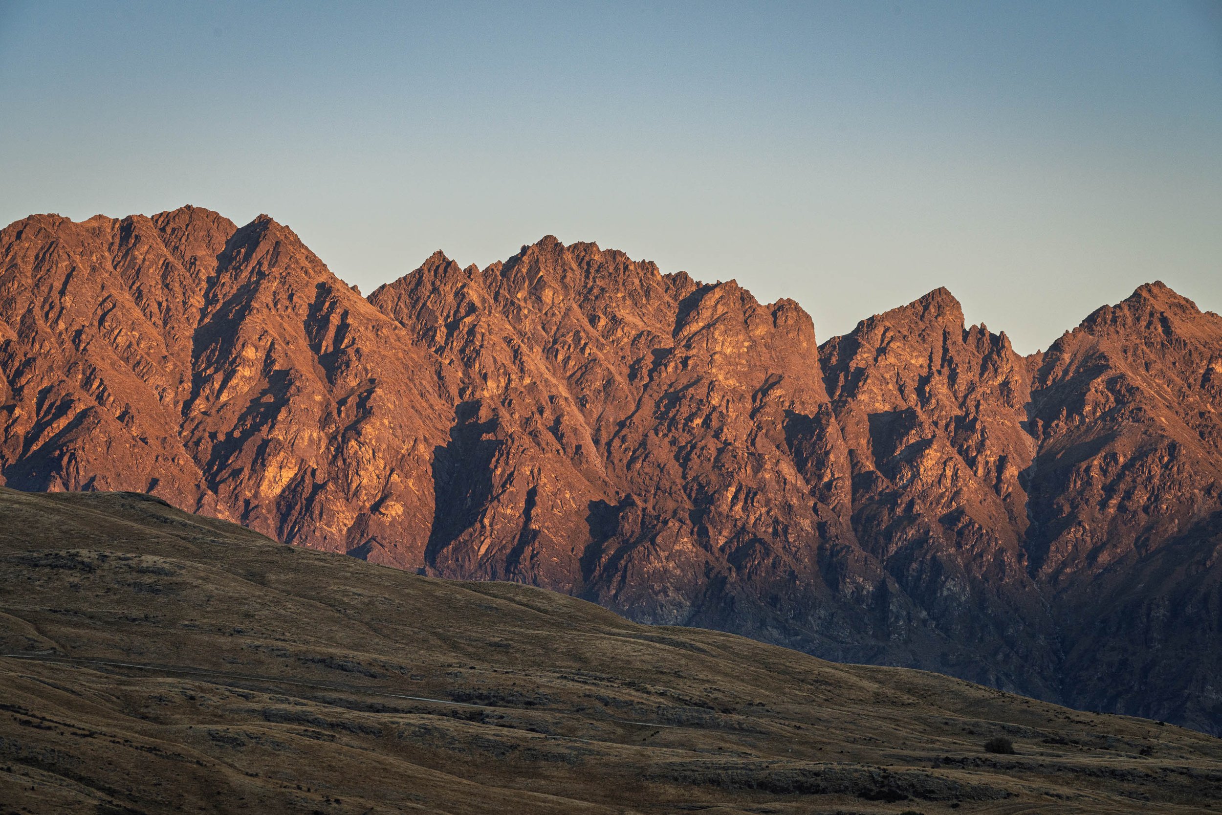 Sunset-lit mountain range above rolling grassy hills.