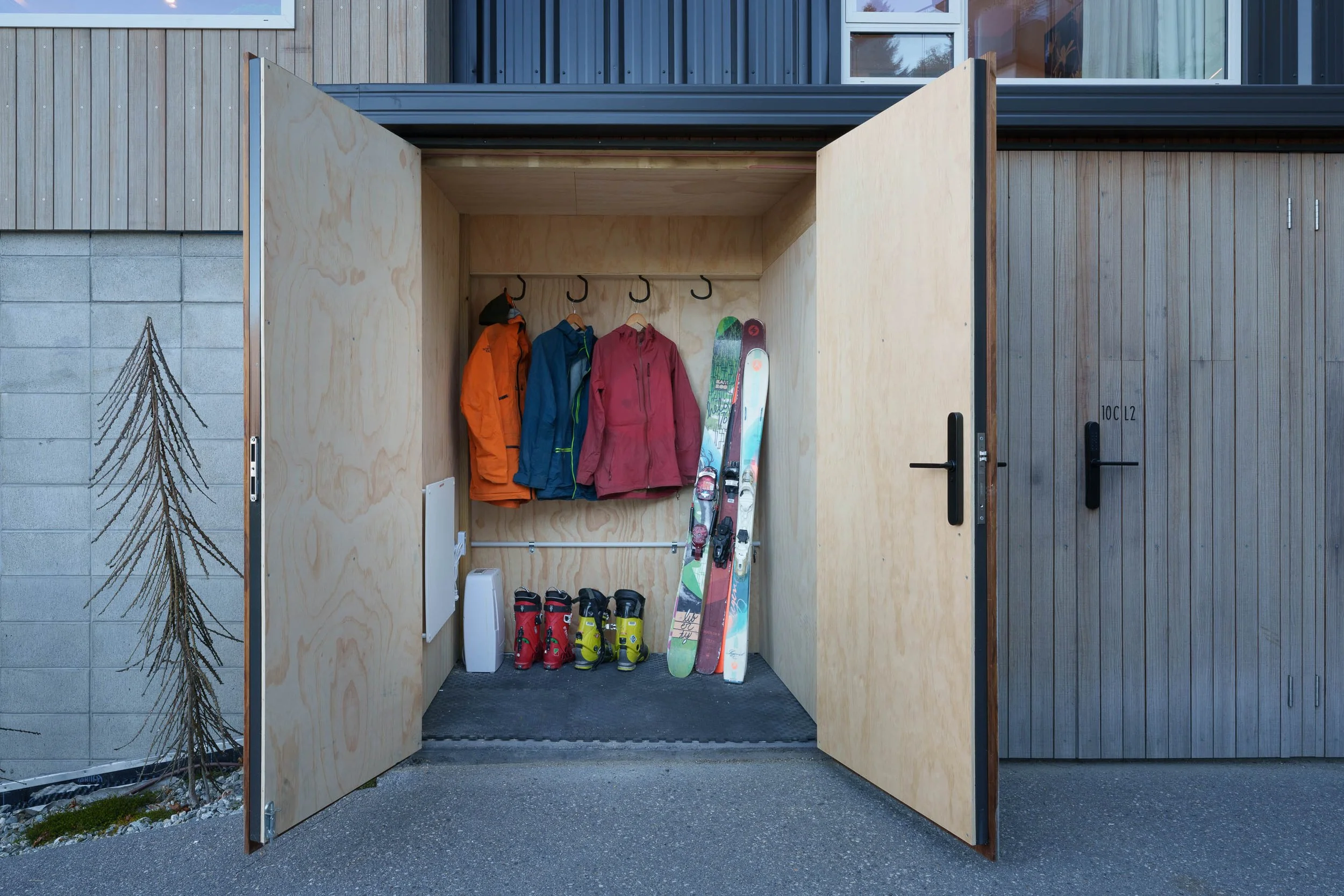 Outdoor ski and snowboard storage shed with jackets, skis, and ski boots inside