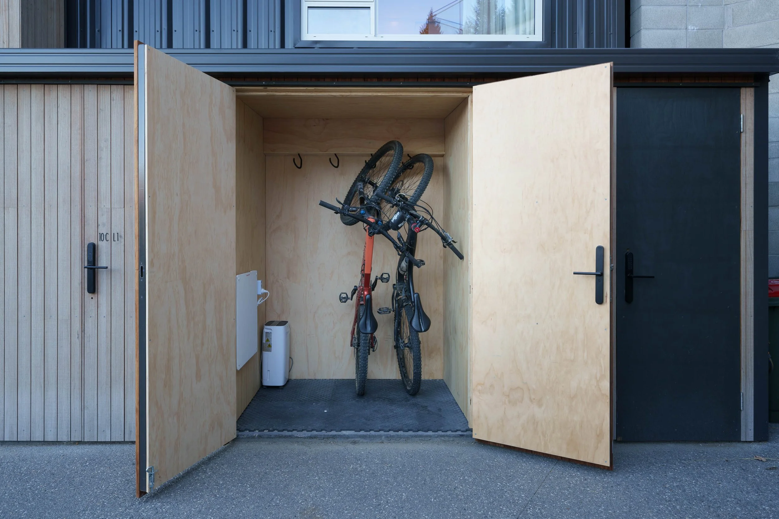 Wooden outdoor bike storage with two bicycles parked inside on hooks.