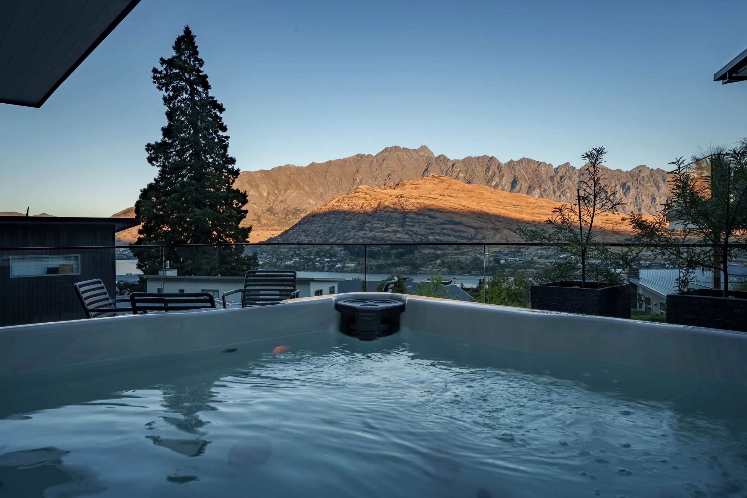 Hot tub on a patio with scenic mountain view, patio furniture, potted plants, and a clear sky in the background.