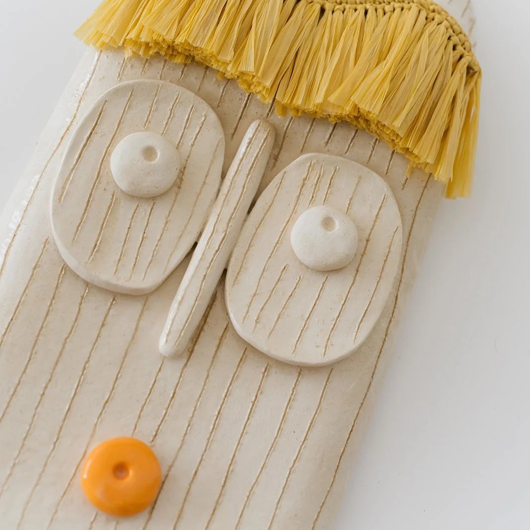 Solara handmade ceramic wall mask with natural raffia fringe and expressive orange lips detail
