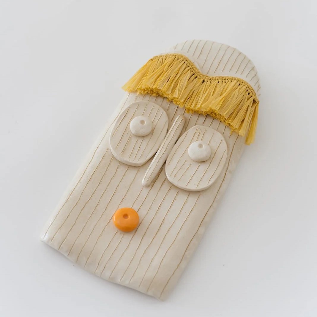 Solara handmade ceramic wall mask with natural raffia fringe and expressive orange lips detail