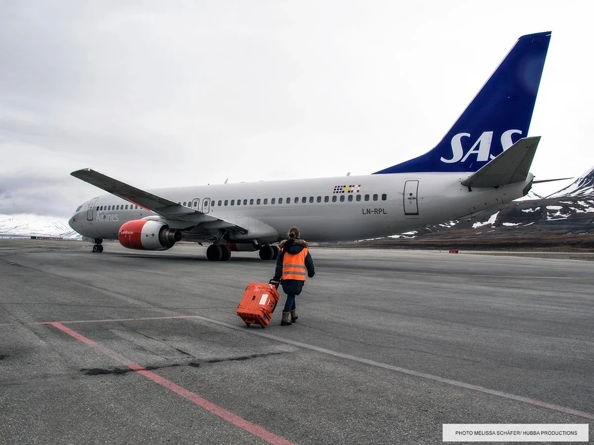 Explorer-koffert brukt i luftfartsoperasjoner foran et SAS-fly på flyplassen, med bakkepersonell i arbeid.