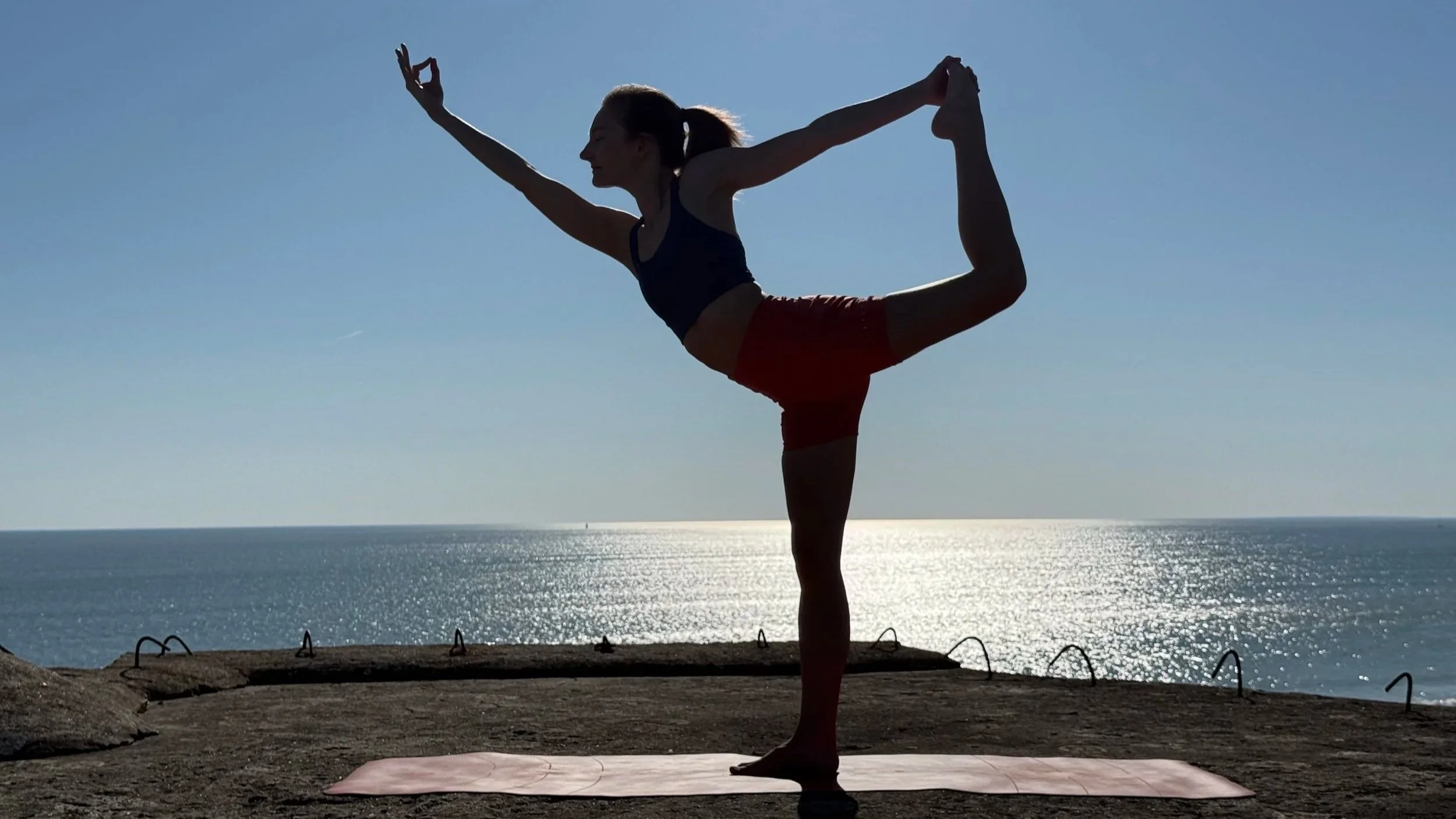 Femme pratiquant le yoga dans une pose d'équilibre sur la plage avec vue sur l'océan au coucher de soleil