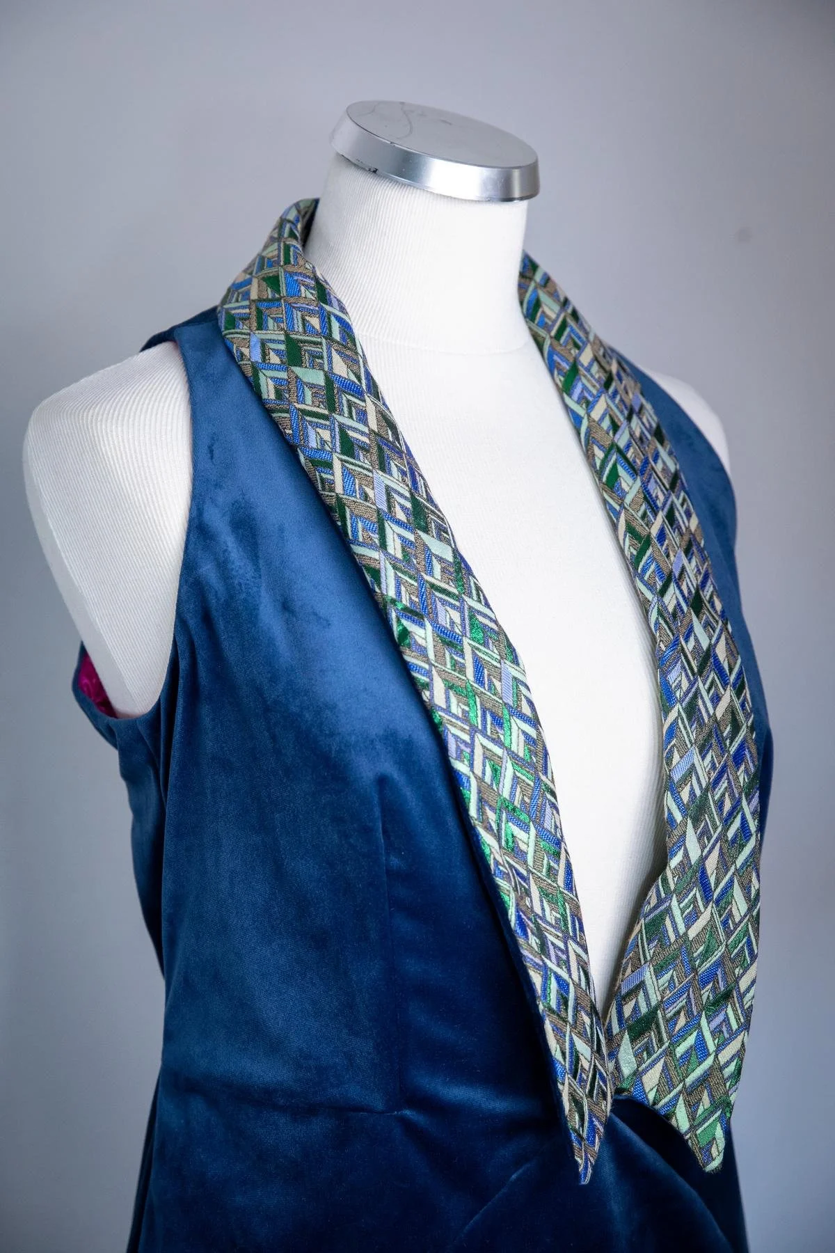 A mannequin wearing a blue vest with a patterned scarf draped around its neck.
