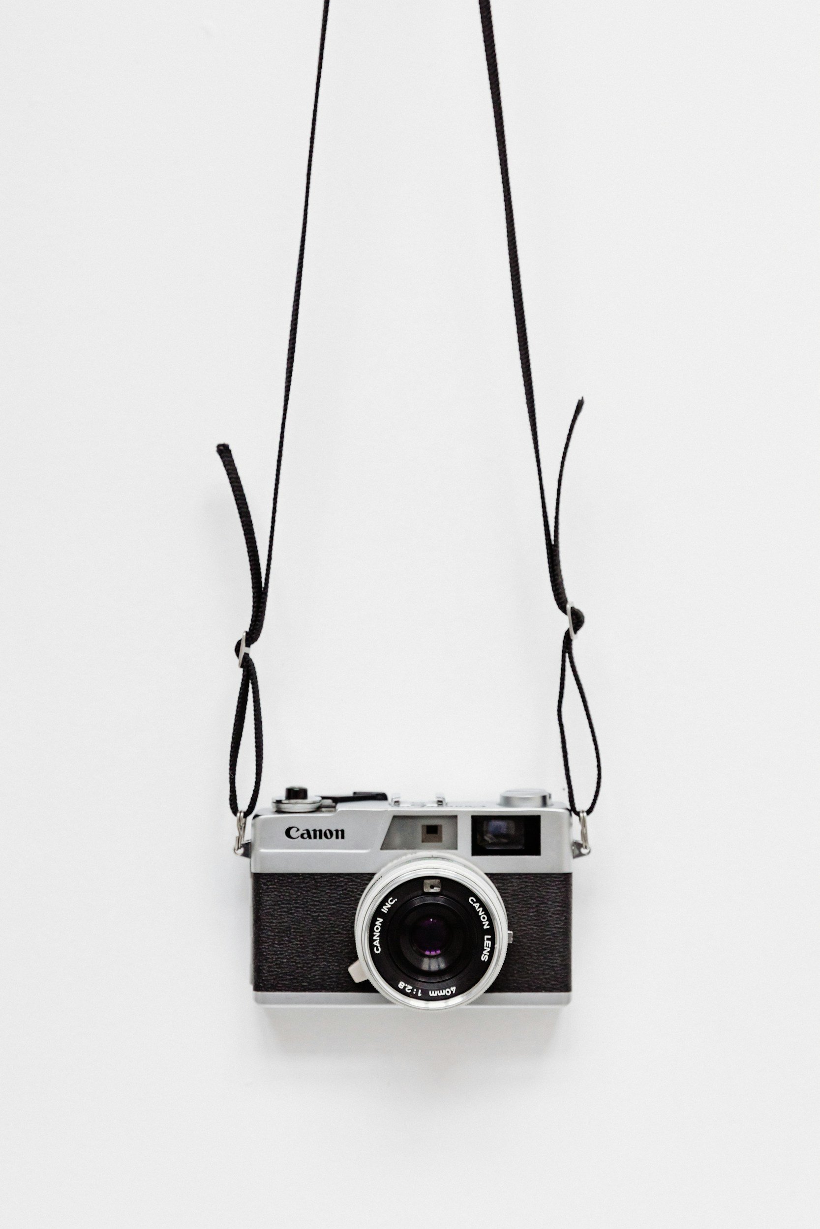 Un appareil photo Canon suspendu par une lanière noire contre un fond blanc.