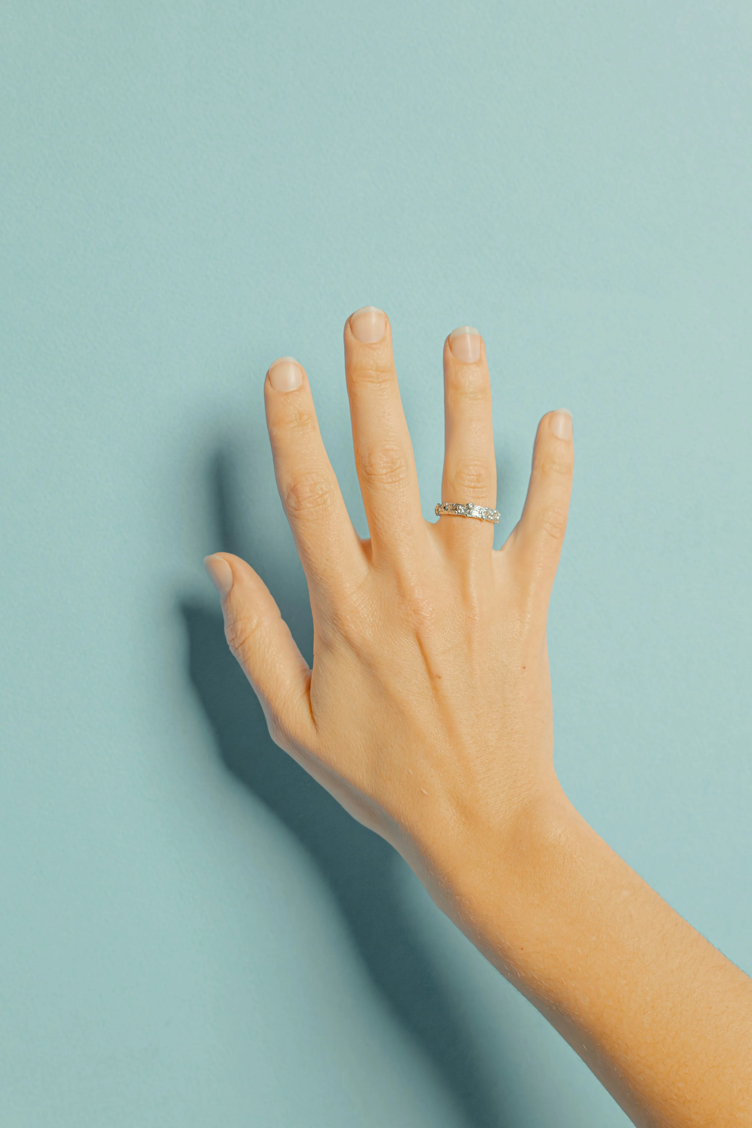 A hand showing a ring on the ring finger against a blue background.