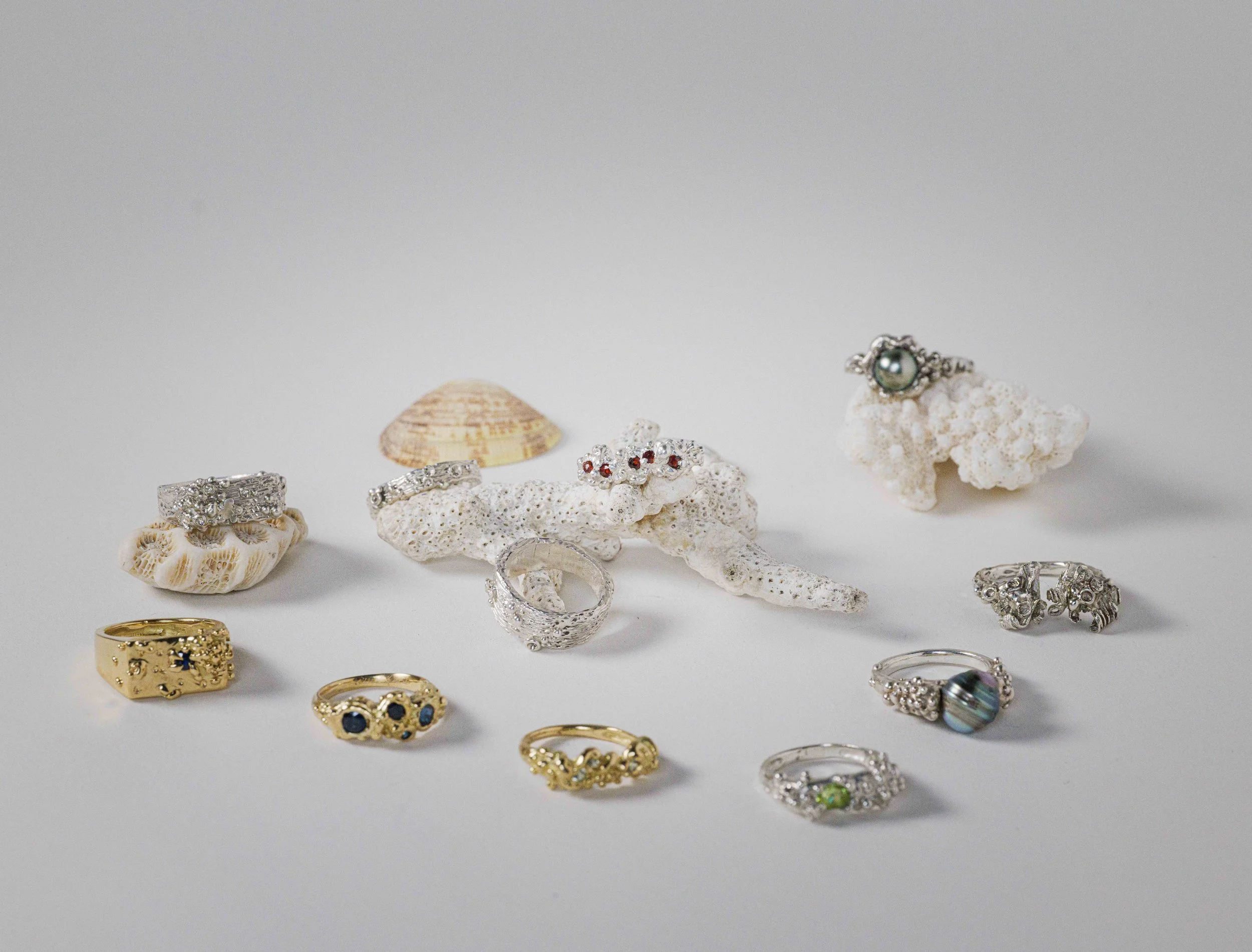 Collection of jewelry rings placed on a white surface, with white coral and seashells as decoration.