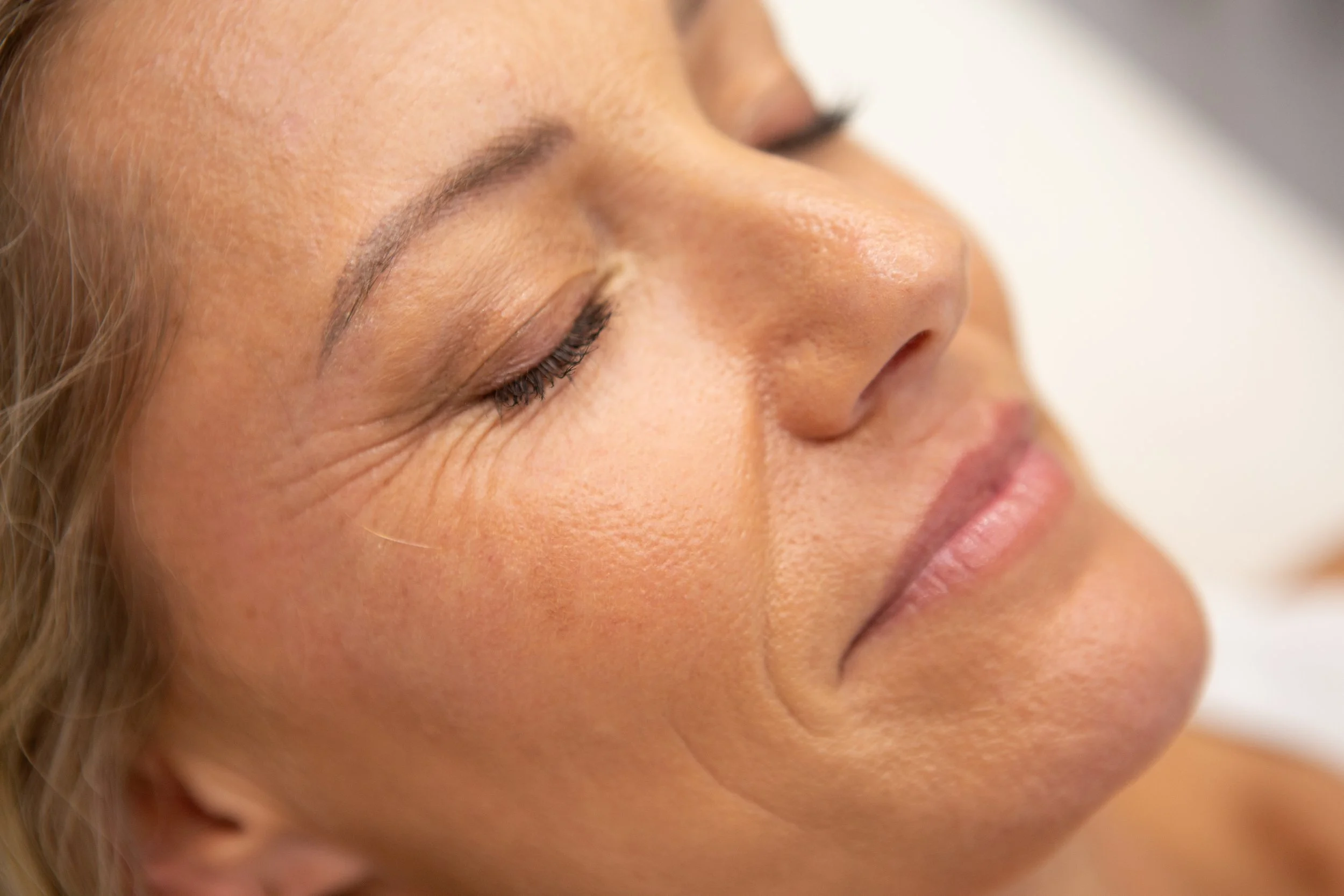 Close-up of a woman's face with her eyes closed, showing smooth skin, fine wrinkles, and natural features.