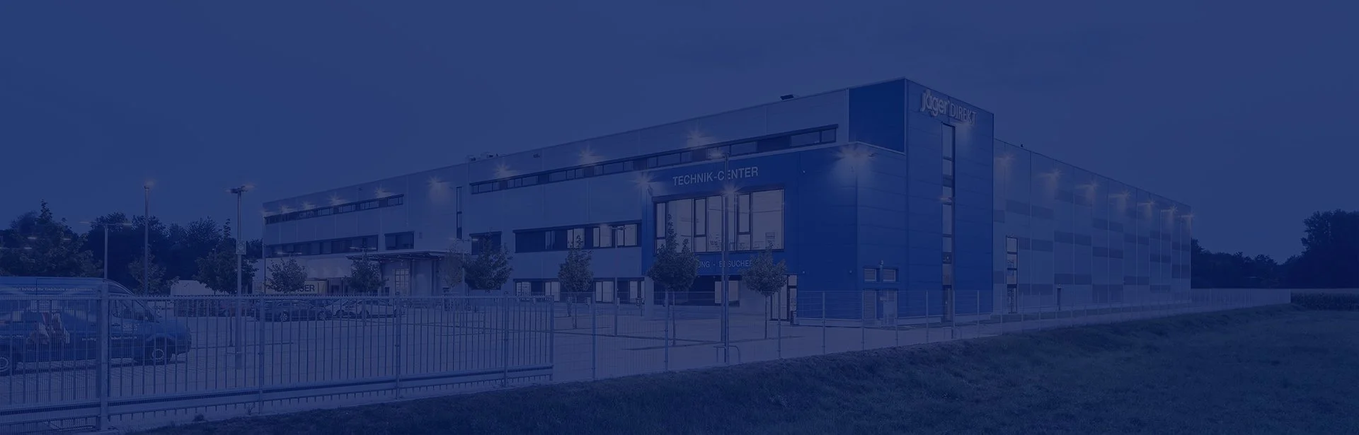 Außenansicht eines modernen Technikzentrums bei Nacht, mit Beleuchtung und Zaun im Vordergrund.