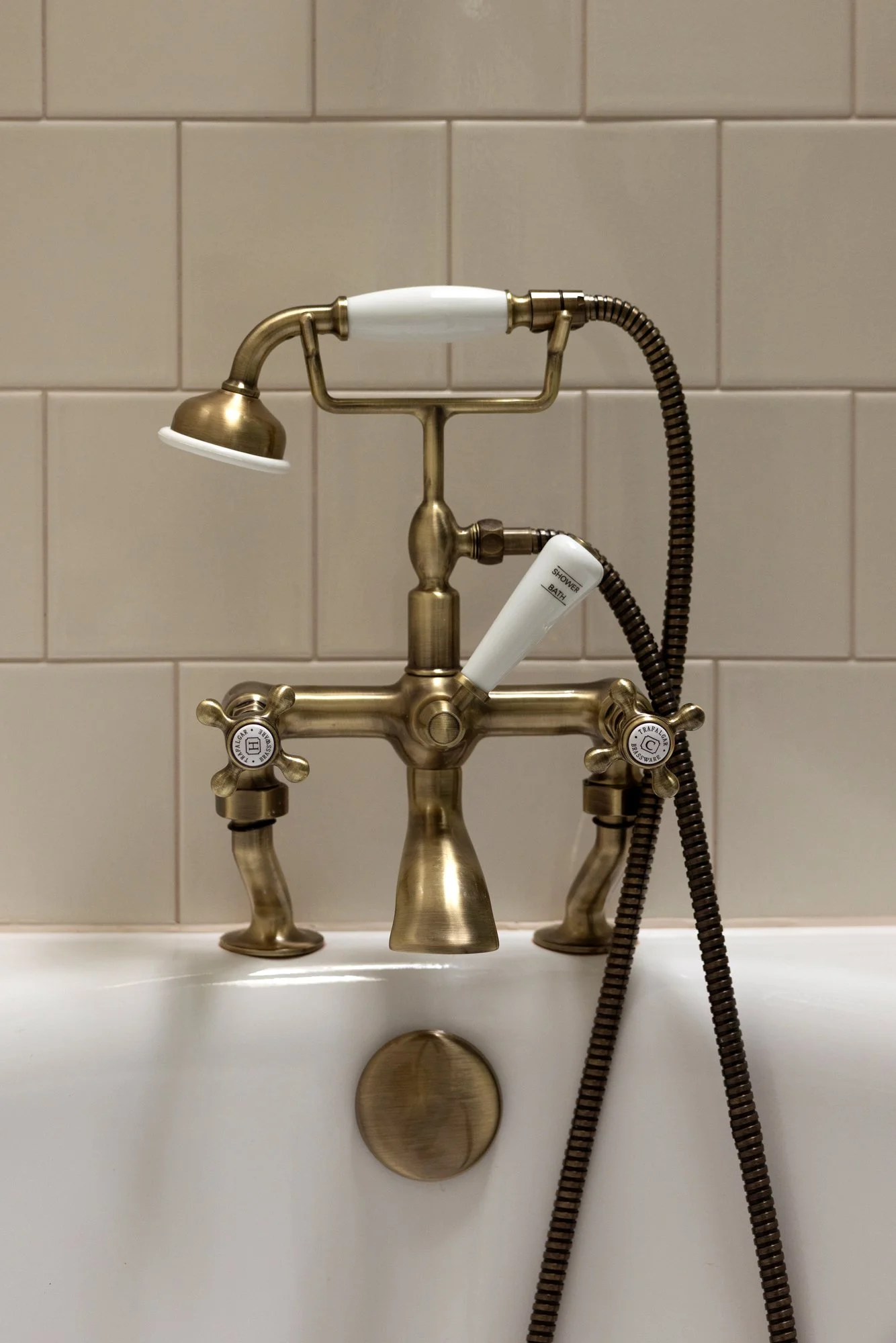 Close-up of a vintage-style brass faucet with a shower head attachment and a white shower handle, mounted on a white ceramic tile wall.