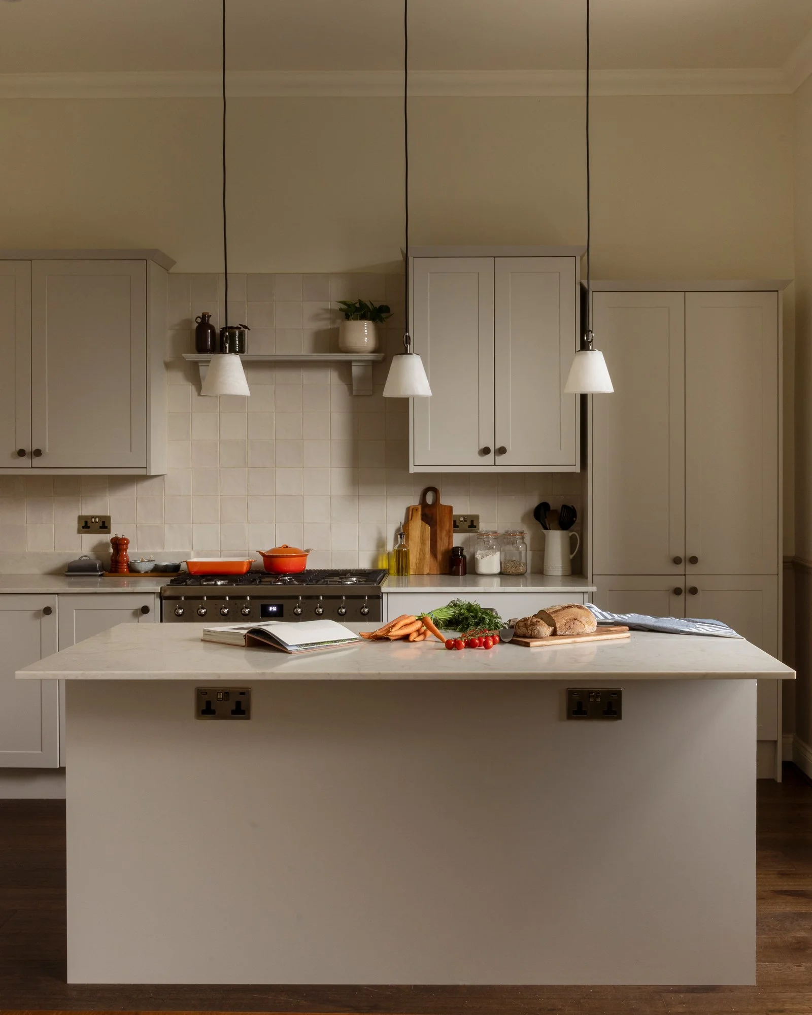 Kitchen with white cabinetry, a countertop with vegetables, bread, a book, and jars, and a kitchen island with two electrical outlets.