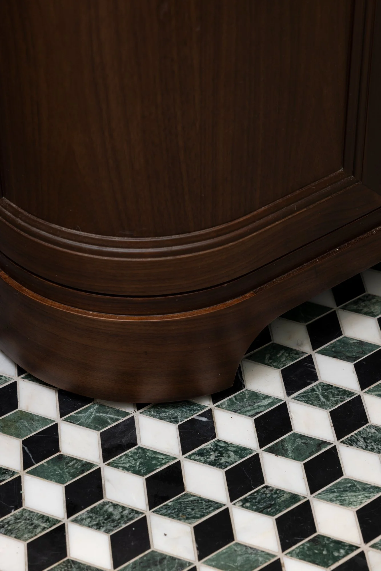 Close-up of a dark wooden curved furniture piece on a black and white hexagonal tile floor.