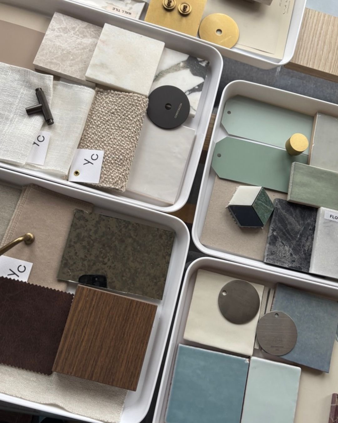 Sample tiles, countertop materials, and hardware samples in various colors and textures laid out in trays for interior design selection.